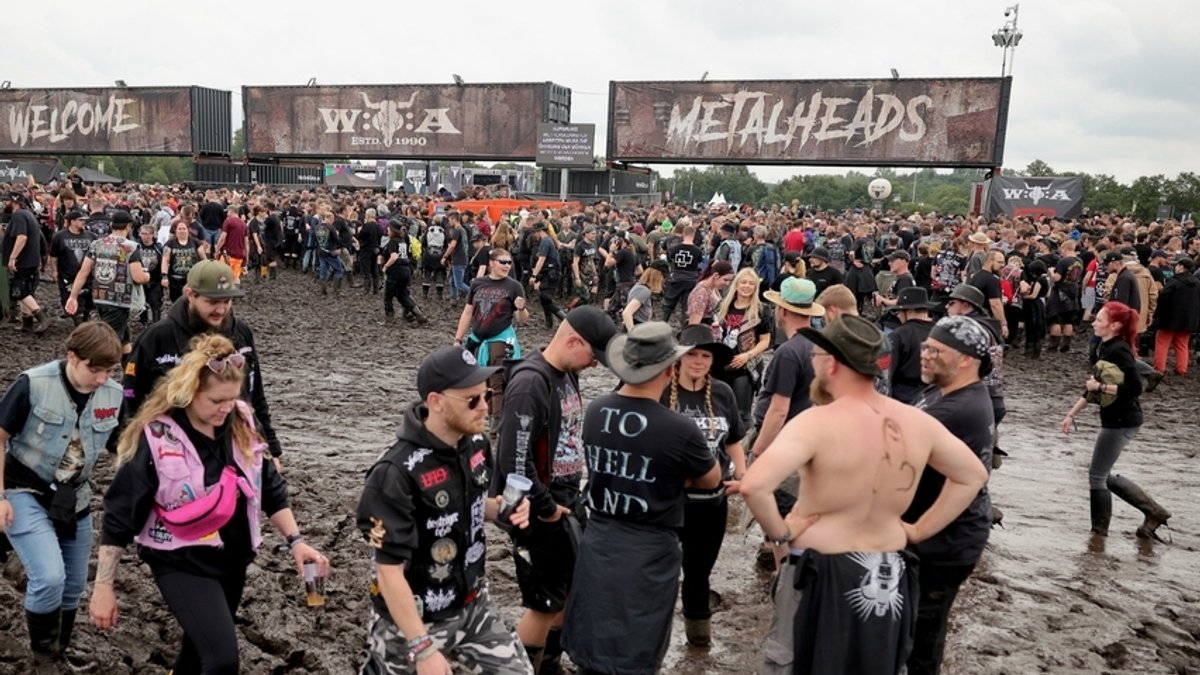 Wacken: Metal-Fans stehen im Schlamm und warten an einem der Eingänge auf die Öffnung des Festivalgeländes.