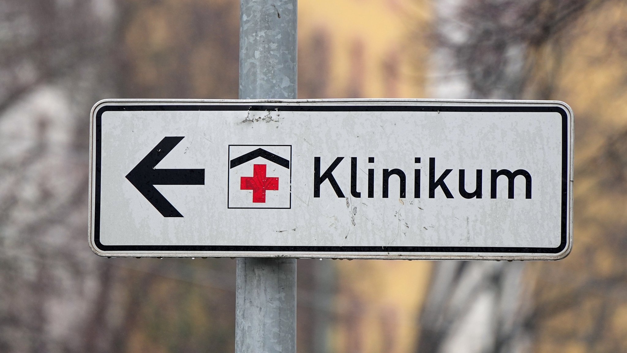 Ein Schild mit rotem Kreuz weist den Weg zu einem Klinikum.