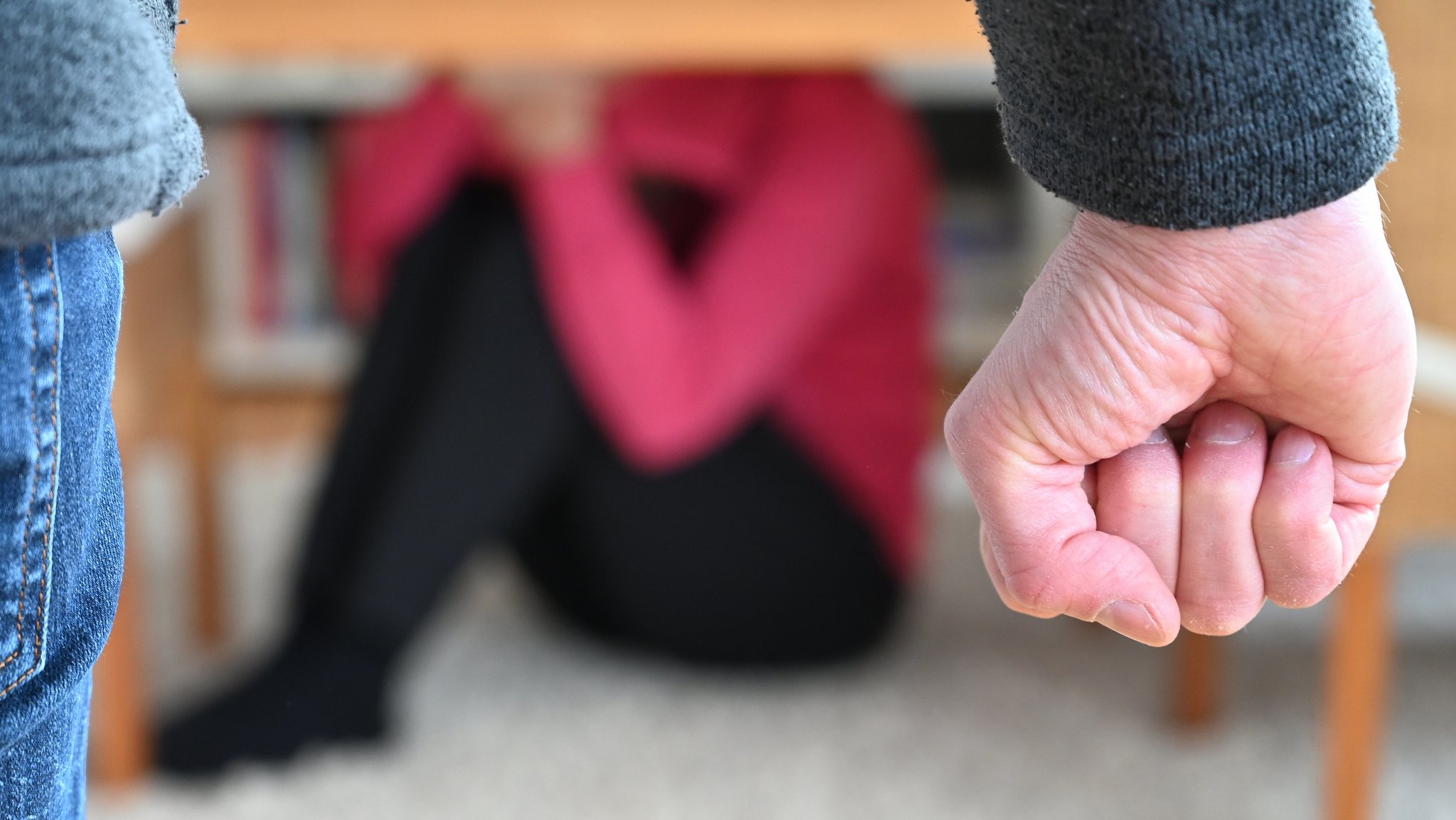 Frau sitzt zusammengekauert am Boden, Mann ballt die Faust