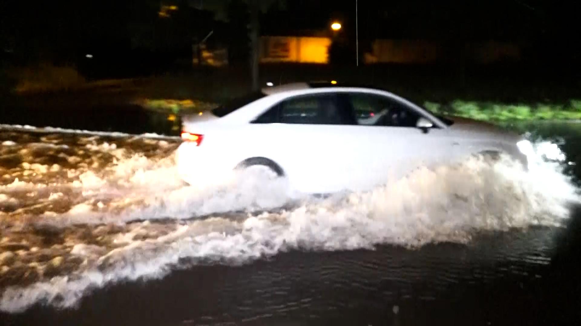 Ein Auto fährt über eine überschwemmte Straße.