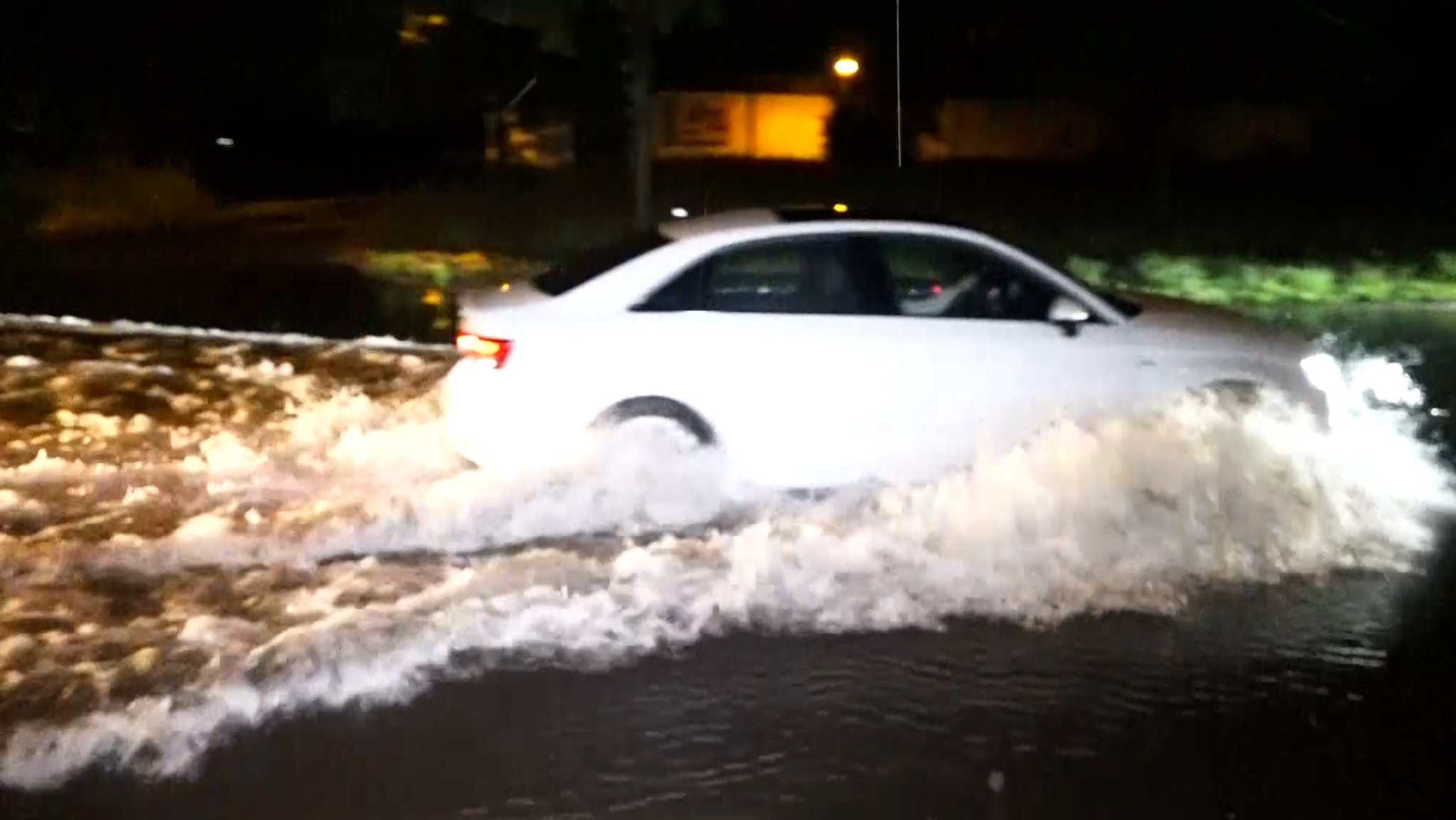 Ein Auto fährt über eine überschwemmte Straße.