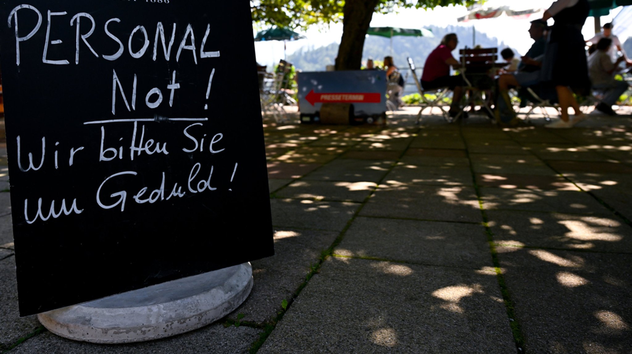 Auf einem Schild in einem Gartenlokal steht: Personalnot! Wir bitten Sie um Geduld!