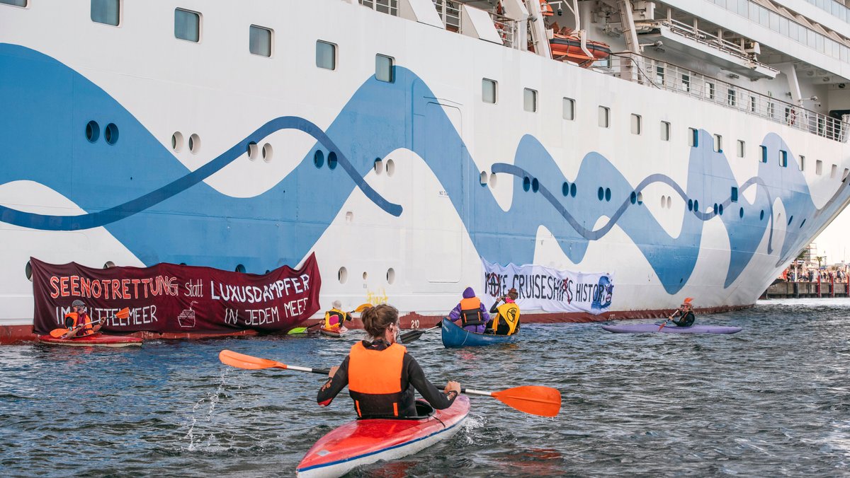 Klimaaktivisten versuchen auf Kanus und aufblasbaren Booten ein Kreuzfahrtschiff am Auslaufen zu hinder