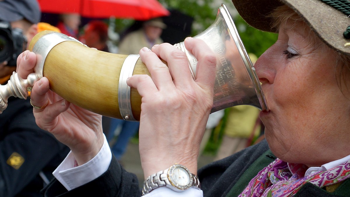 Eine Frau trinkt Starkbier aus einem Horn. 