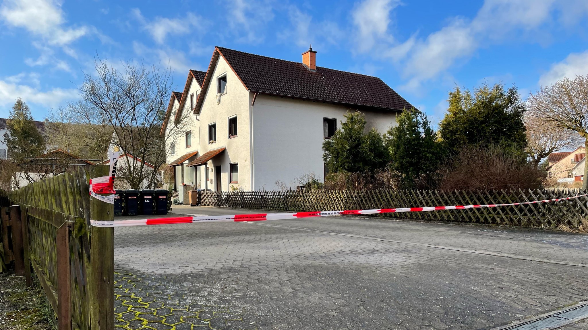 Rot-weißes Absperrband der Polizei an einer Hauseinfahrt, im Hintergrund mehrere Häuser.