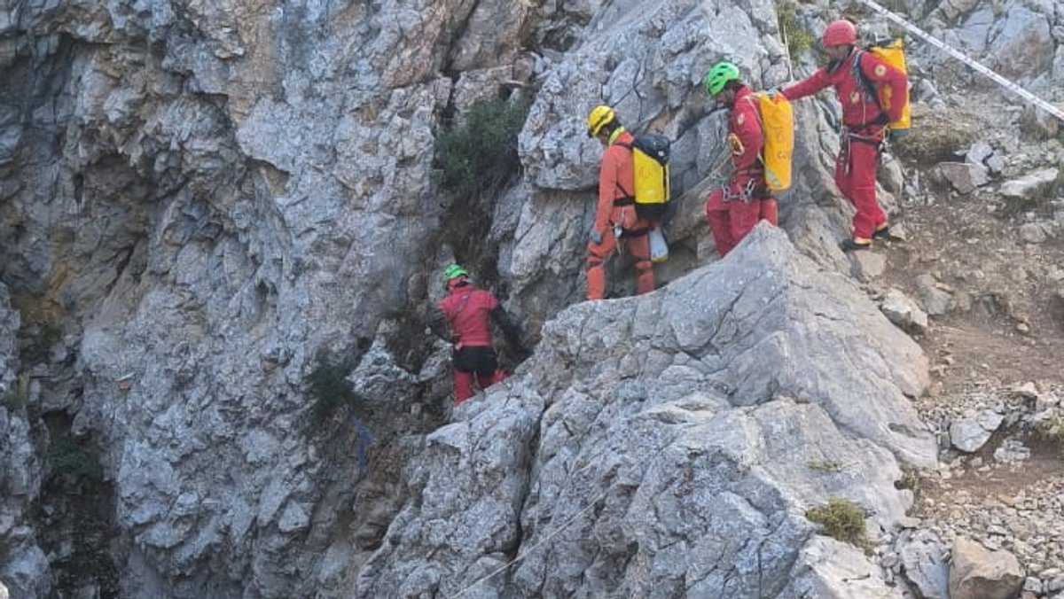 Ein Rettungsteam in roten und orangenen Overalls, mit Helmen und Packsäcken steigt in Morca-Höhle in der Südtürkei.