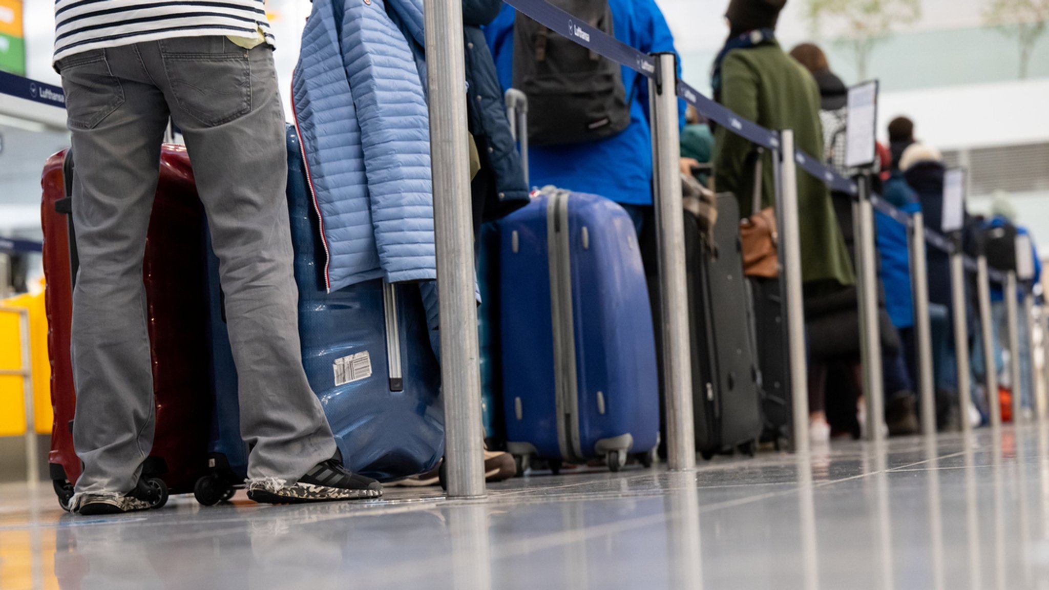 Passagiere stehen mit ihrem Gepäck an Check-in-Schaltern am Flughafen München (Archivbild).