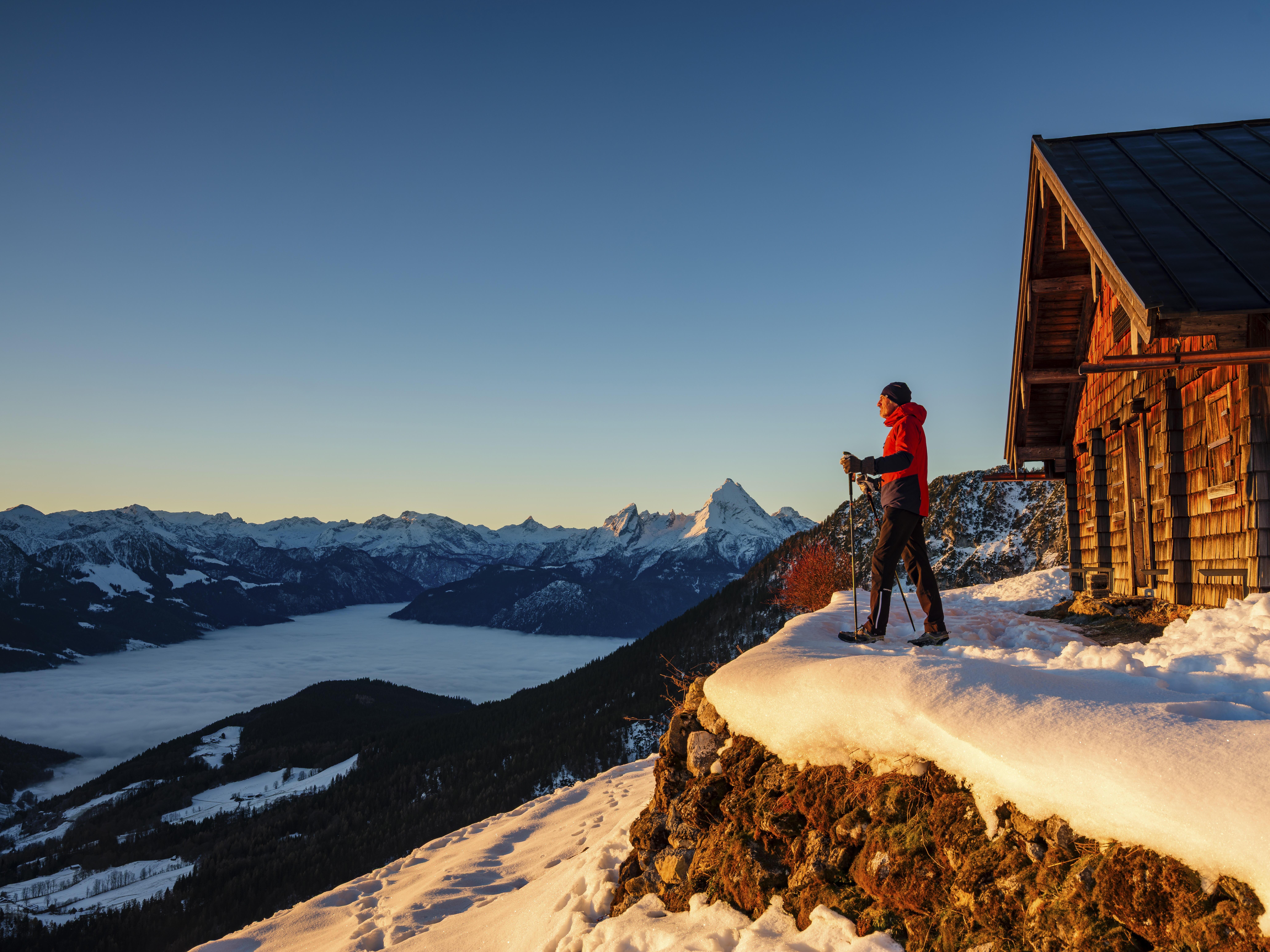 Winterwanderer vor holzgeschindelter Hütte, Nebel im Tal, im Hintergrund der Watzmann.