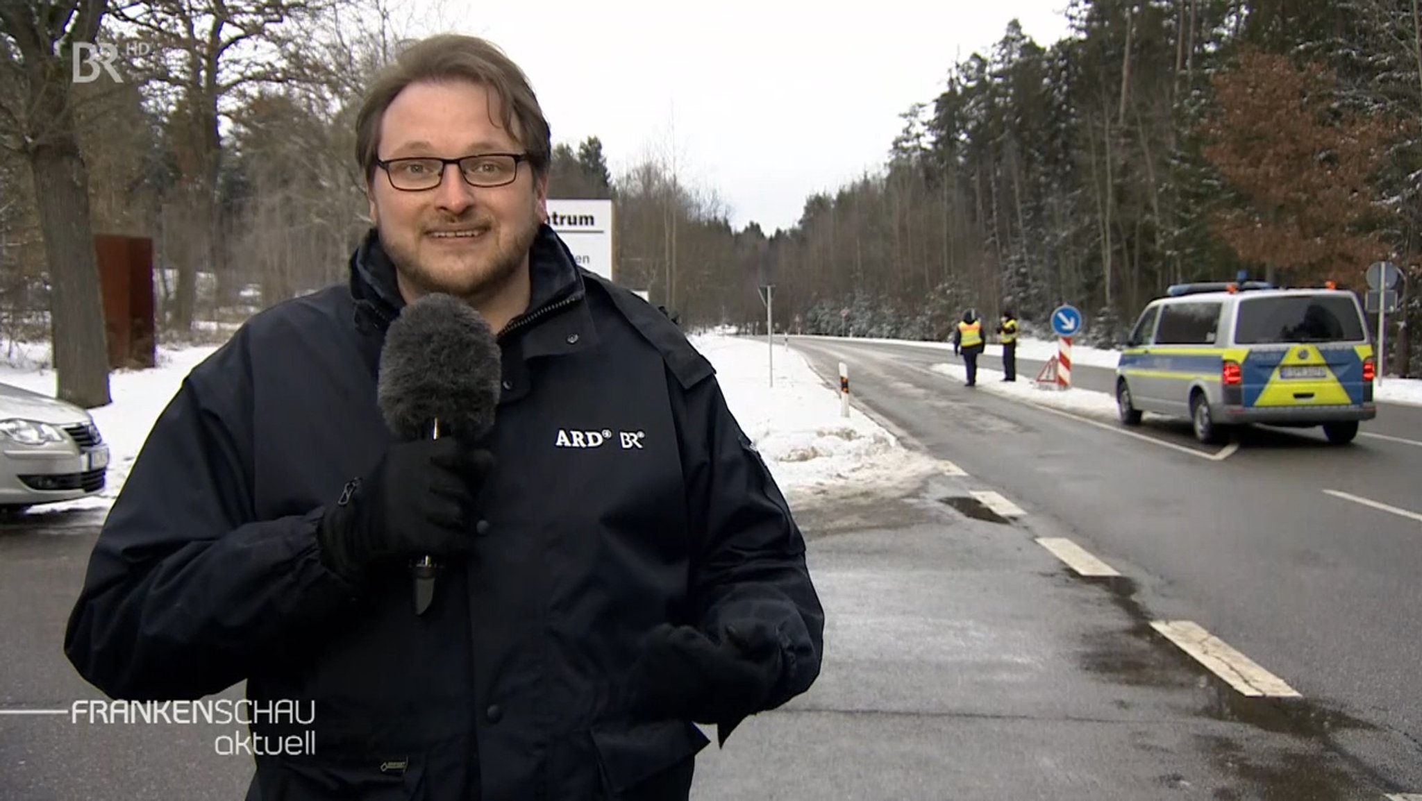 Ein BR-Reporter berichtet von den Grenzkontrollen, im HIntergrund sind Polizisten zu sehen.