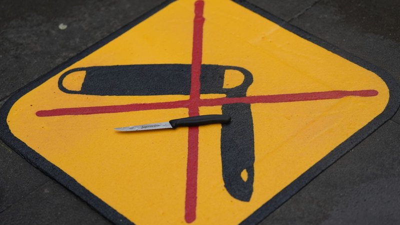 Auf einem Schild, das auf eine Messerverbotszone hinweist, liegt ein Messer. | Bild: dpa-Bildfunk/Marcus Brandt Auf einem Schild, das auf eine Messerverbotszone hinweist, liegt ein Messer.