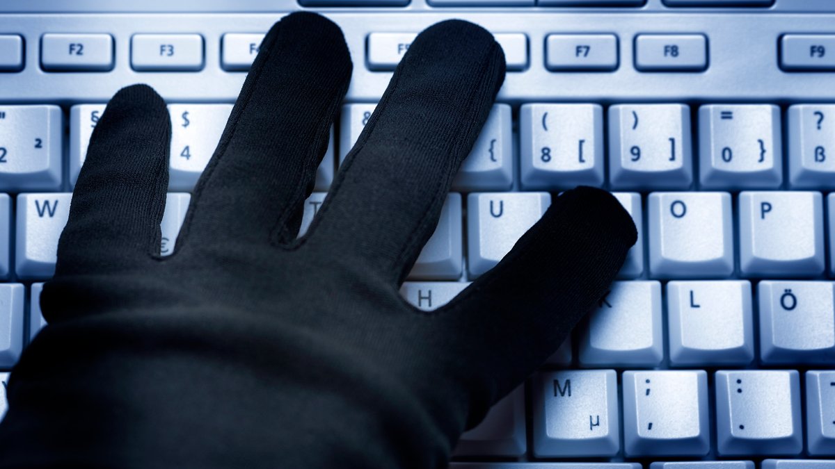 Eine Hand mit schwarzem Handschuh auf einer Computertastatur.