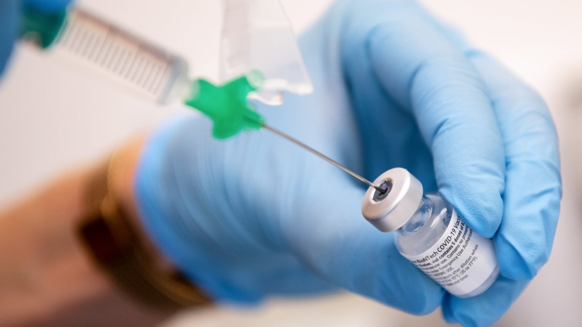 Ein medizinischer Mitarbeiter mit blauen Schutzhandschuhen zieht eine Spritze mit Corona-Impfstoff auf.
