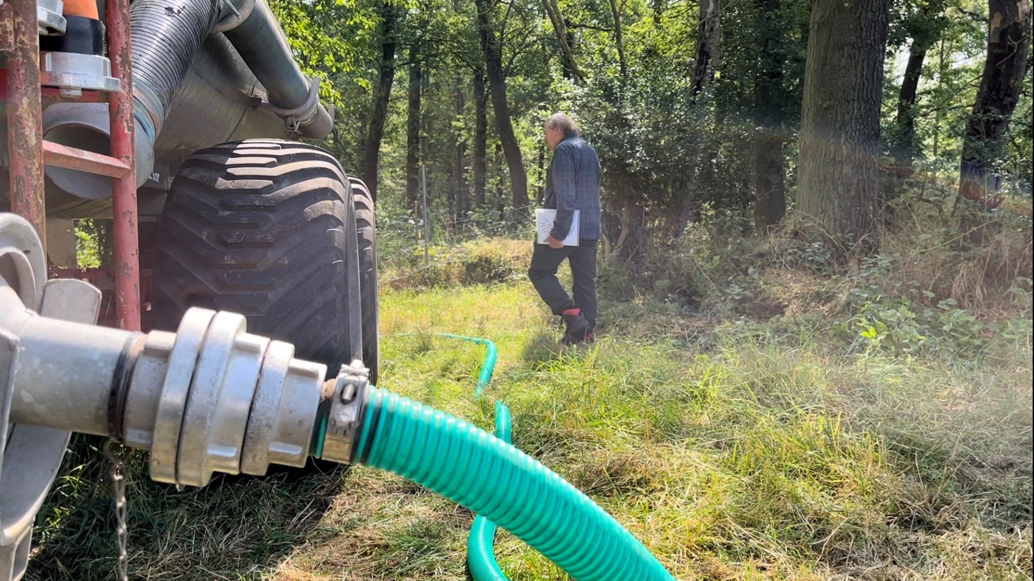 Vorne ein Wasserfass, in dem ein Schlauch steckt, der die 10.000 Liter in die Baumreihen pumpt.