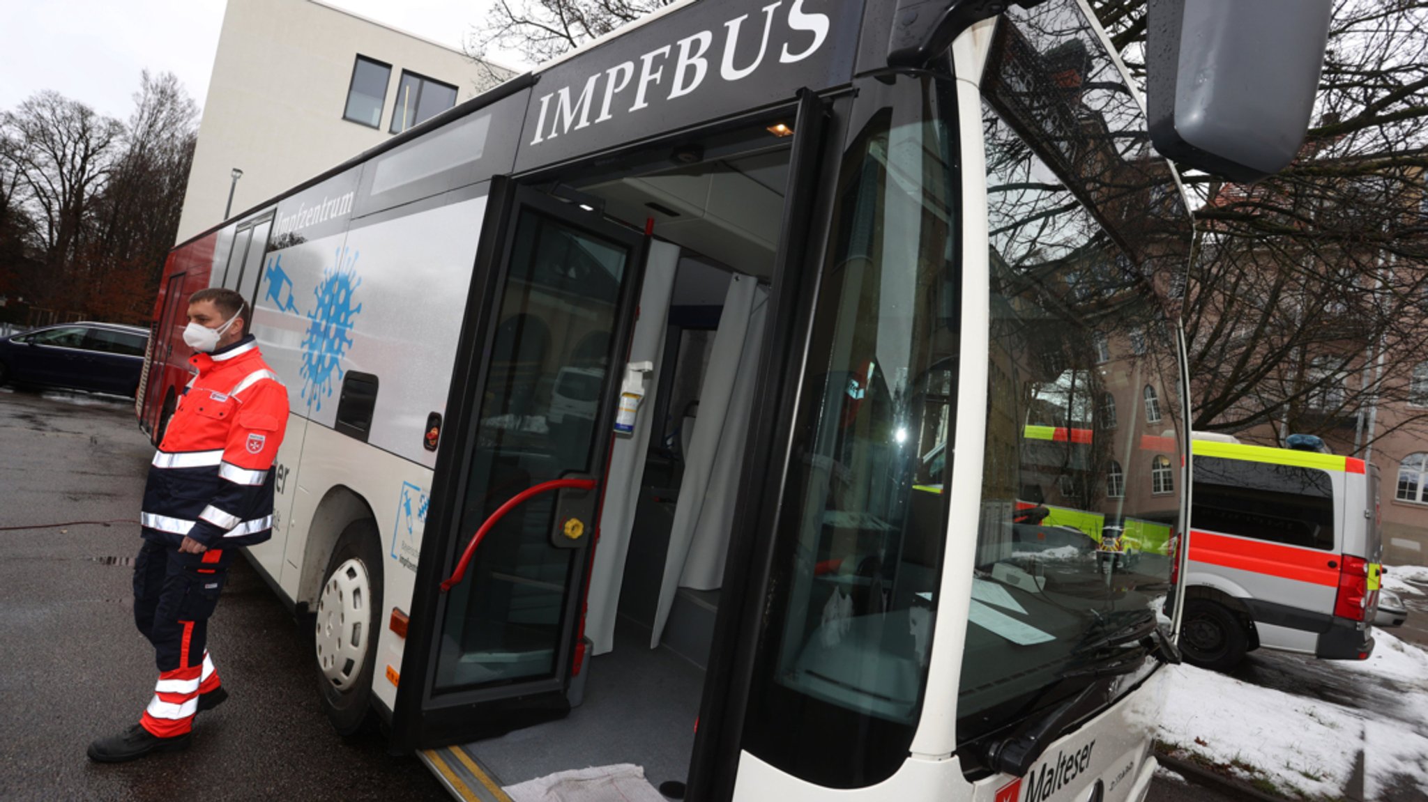 Ein Mitarbeiter der Hilfsorganisation Malteser steht am städtischen Impfzentrum in Memmingen vor einem Impfbus.