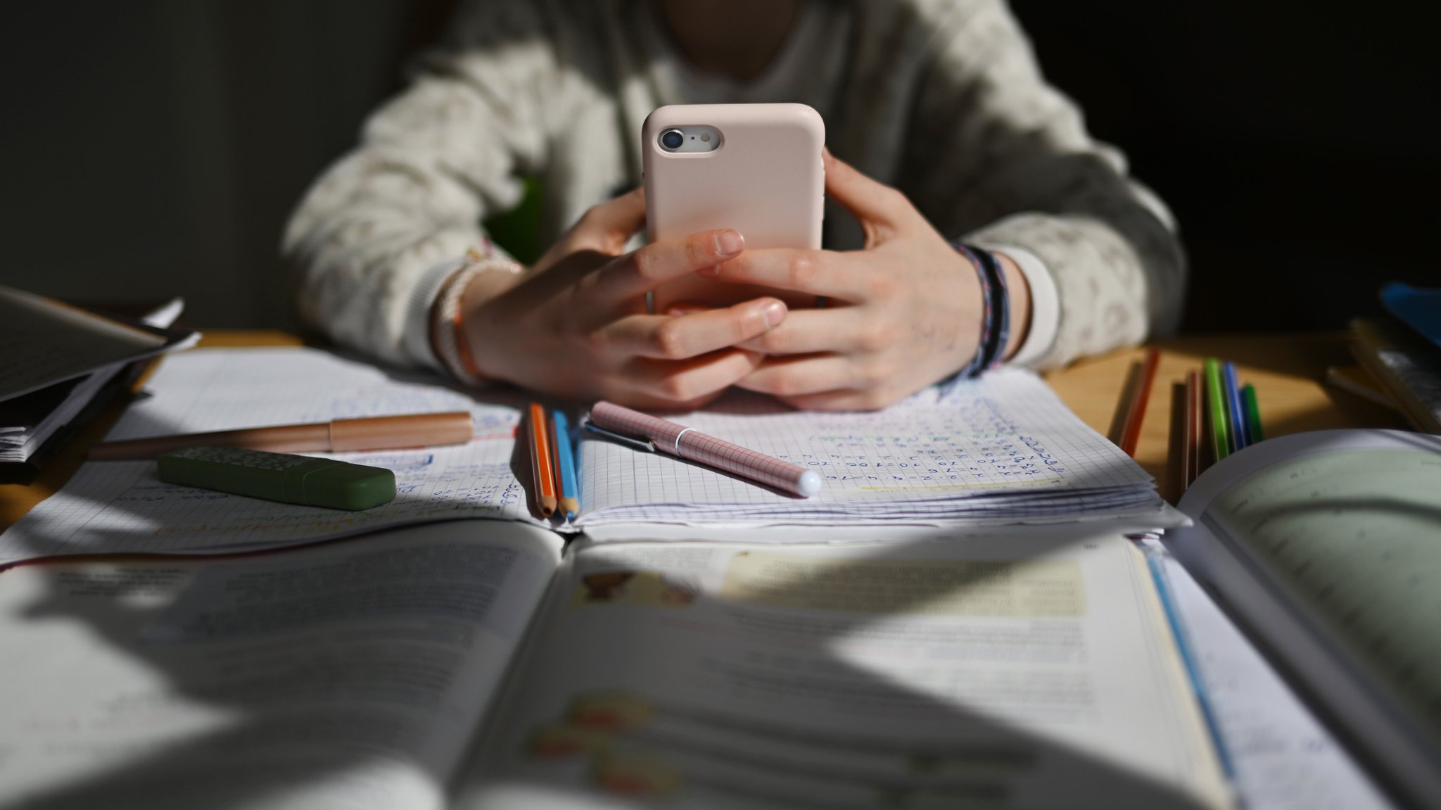 ARCHIV (08.04.2025): Ein Schulkind sitzt an einem Schreibtisch mit Schulmaterialien und hält ein Smartphone in den Händen. (Gestellte Szene). | Bild: picture alliance/dpa | Marijan Murat ARCHIV (08.04.2025): Ein Schulkind sitzt an einem Schreibtisch mit Schulmaterialien und hält ein Smartphone in den Händen. (Gestellte Szene).