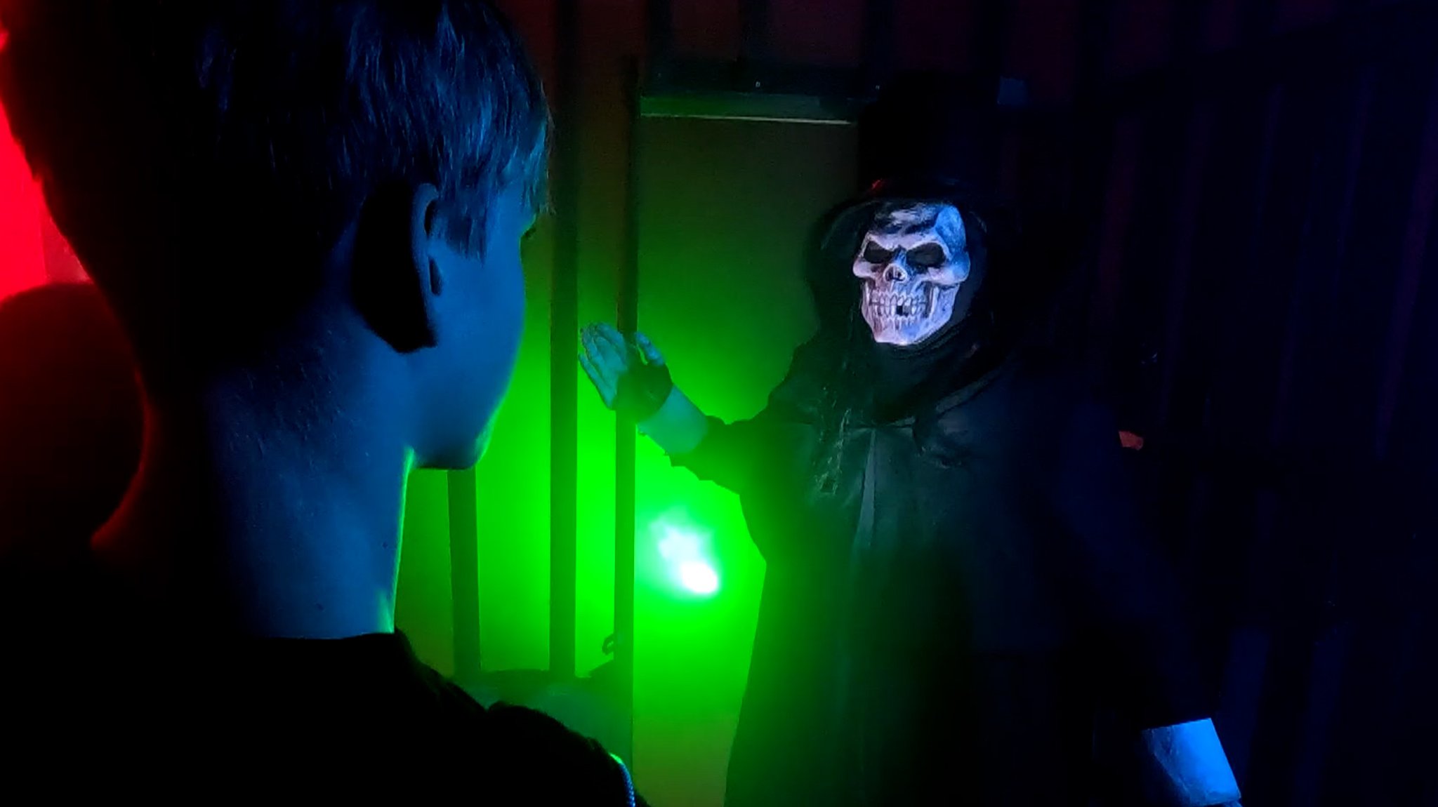 Mit Totenkopfmaske und schwarzem Umhang empfängt der Hausgeist die beiden Kinder im Halloweenhaus.