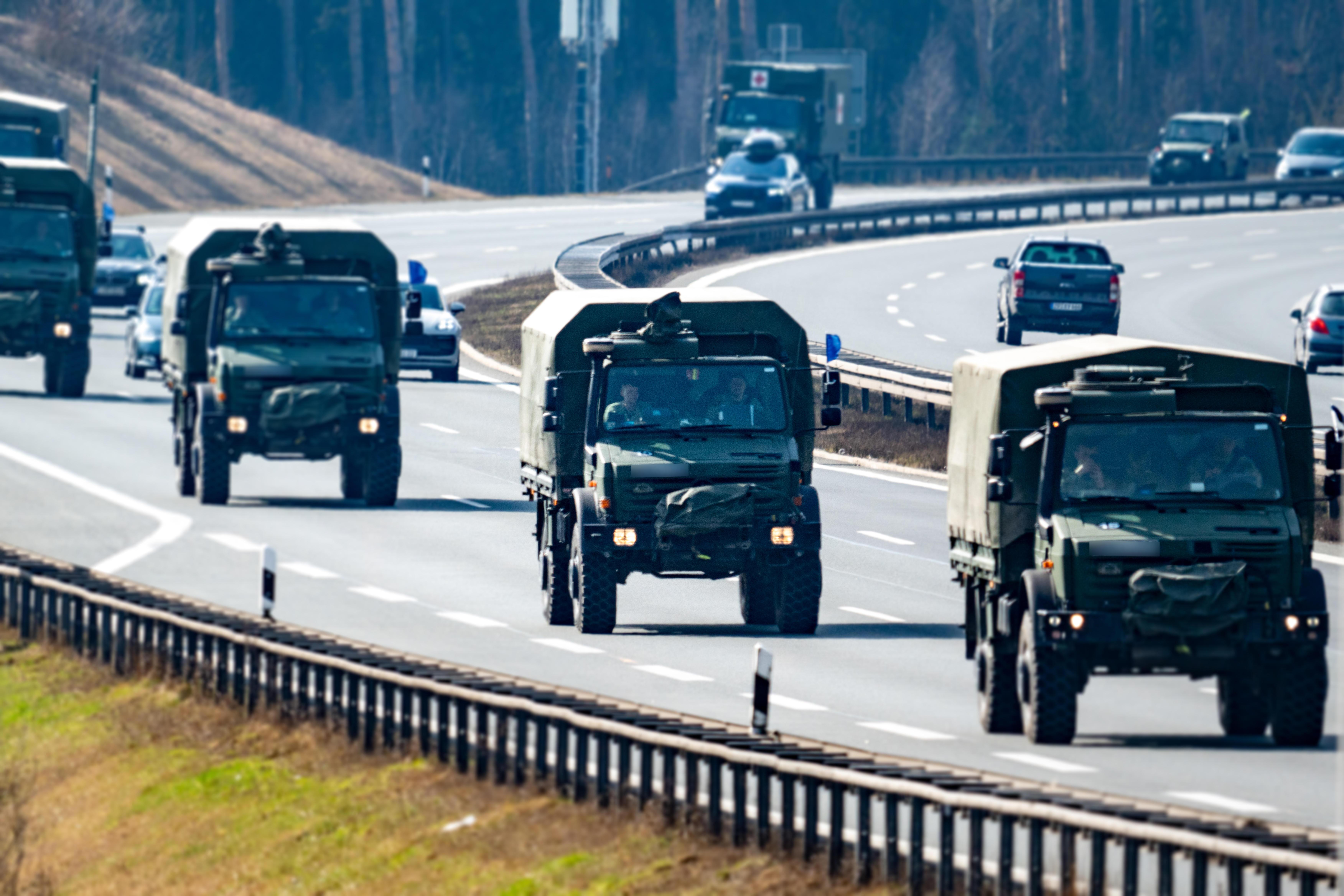 Fünf Militär-LKW mit Tarnabdeckung fahren auf einer Autobahnspur in Kolonne.