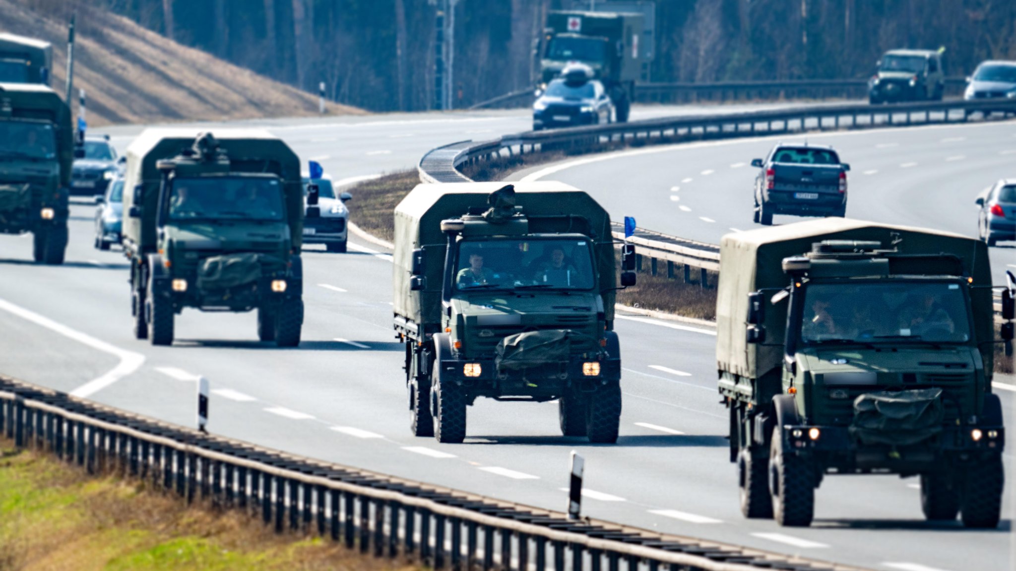 Fünf Militär-LKW mit Tarnabdeckung fahren auf einer Autobahnspur in Kolonne.