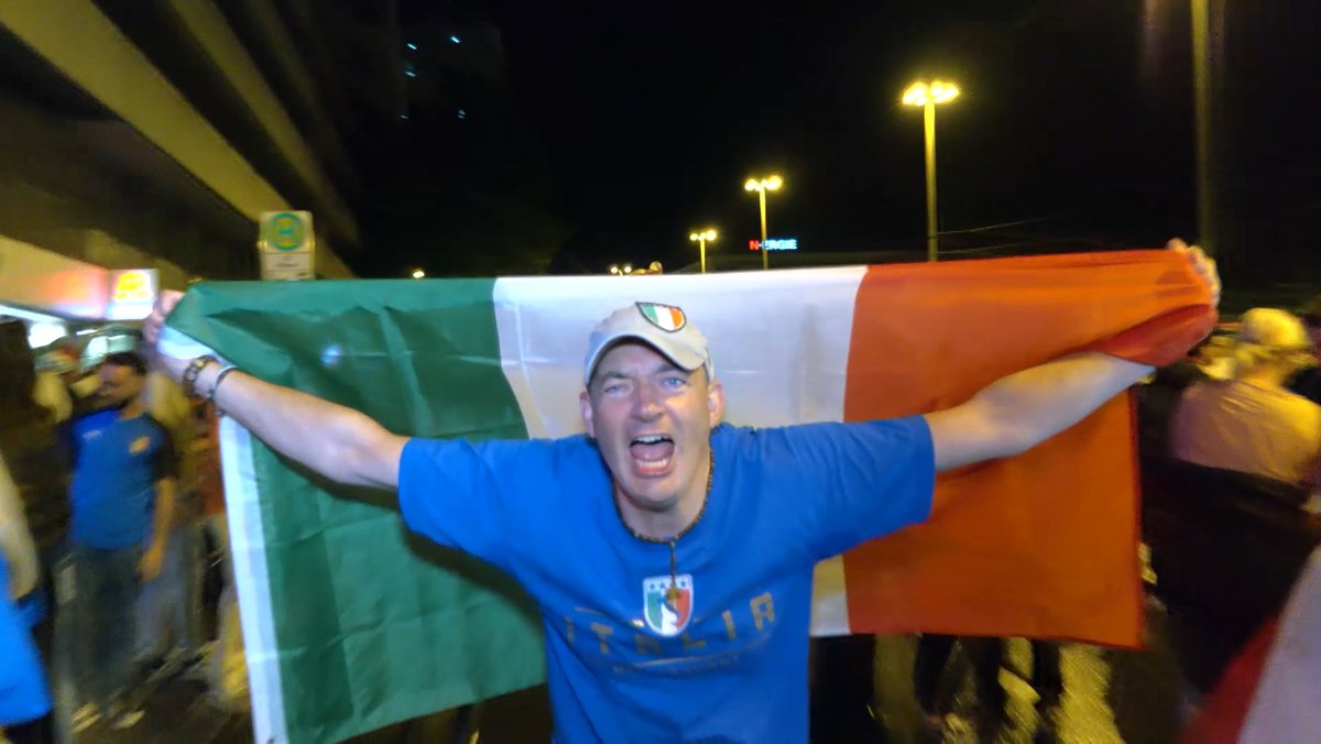 Ein italienischer Fußballfan hält jubelnd eine grün-weiß-rote Italienfahne über sich.