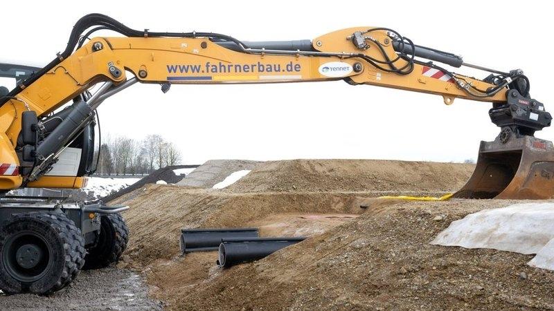 Ein Bagger und zwei aus dem Boden ragende Kabelröhren.