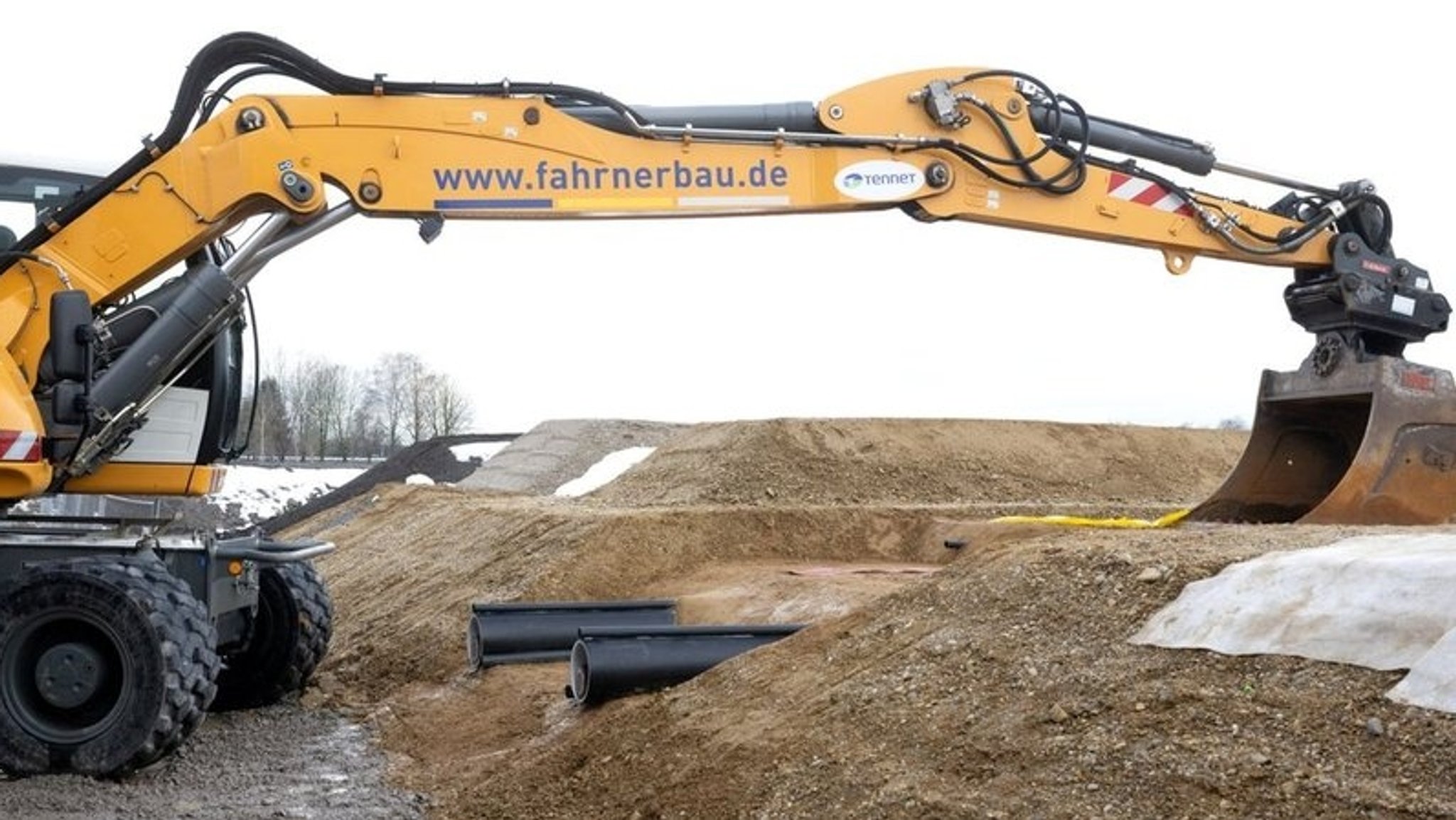 Ein Bagger und zwei aus dem Boden ragende Kabelröhren.