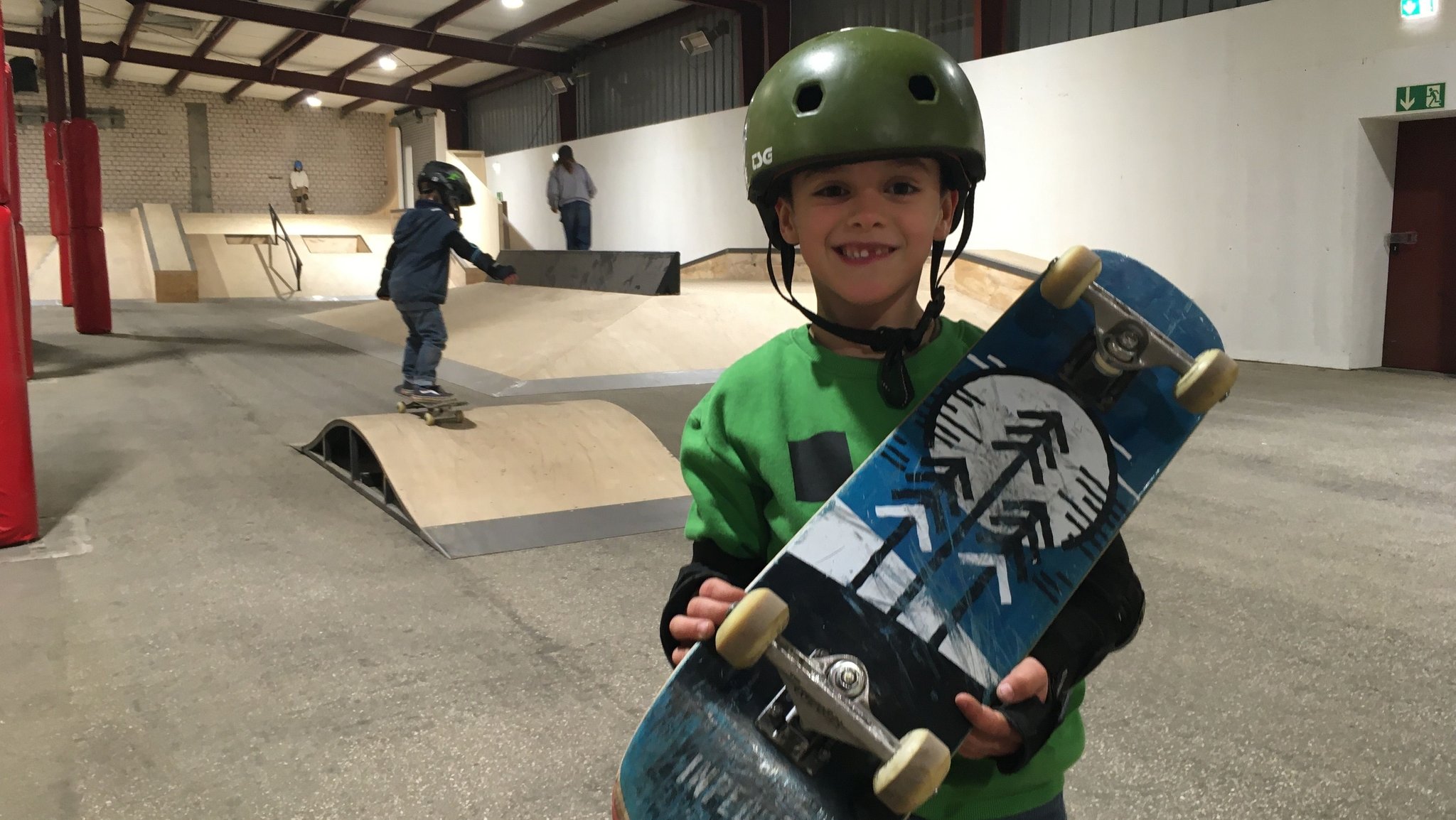 Junge mit Helm auf dem Kopf und Skateboard in der Hand steht in der Skatehalle in Fürth