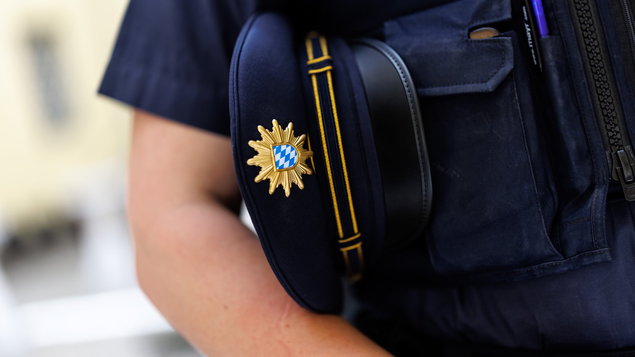 Ein junger Polizist in Ausbildung hält eine Schirmmütze der Bayerischen Polizei unter dem Arm.
