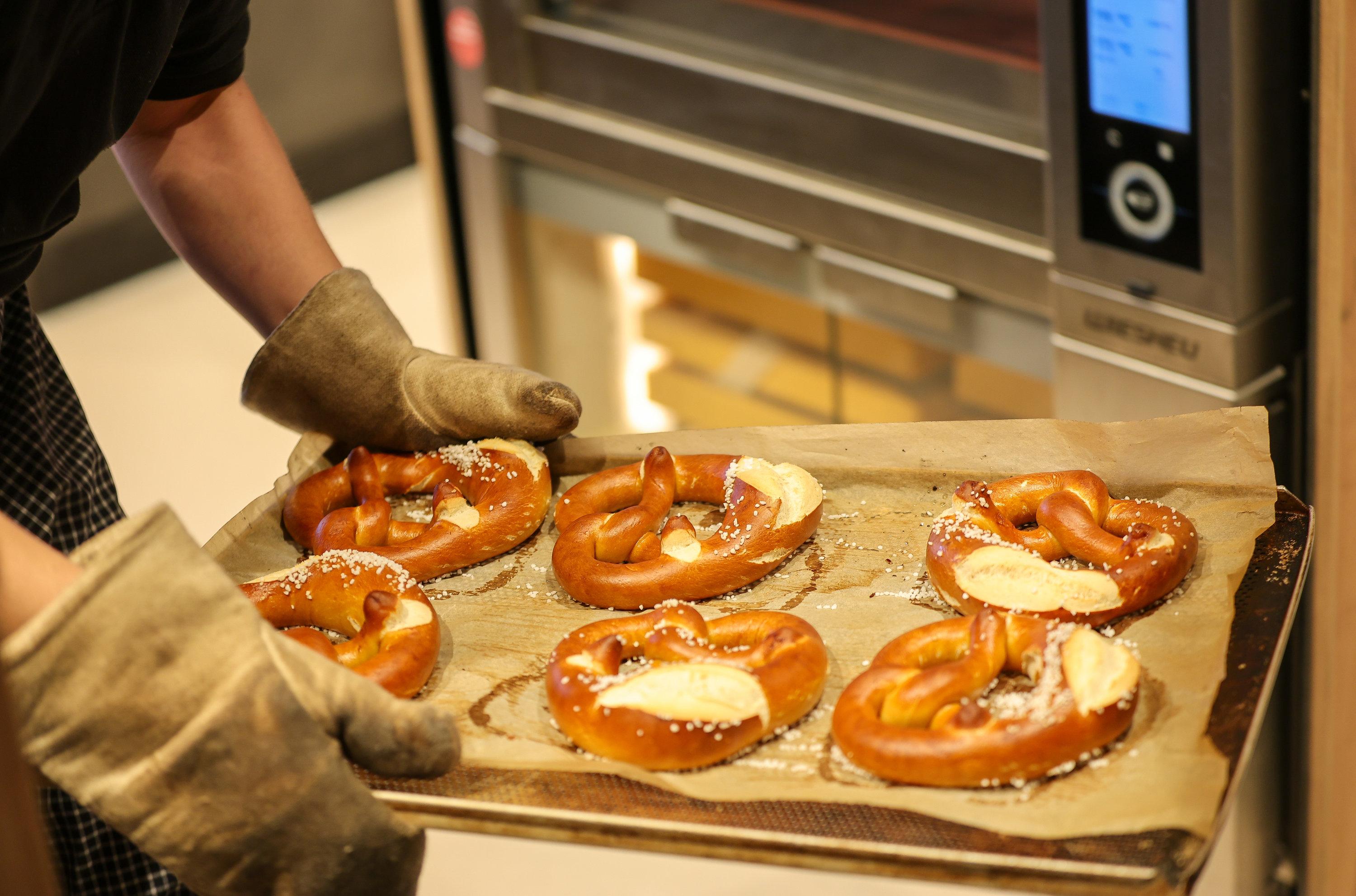 Ein Mitarbeiter nimmt ein Blech mit Brezen aus dem Backofen einer Bäckerei.