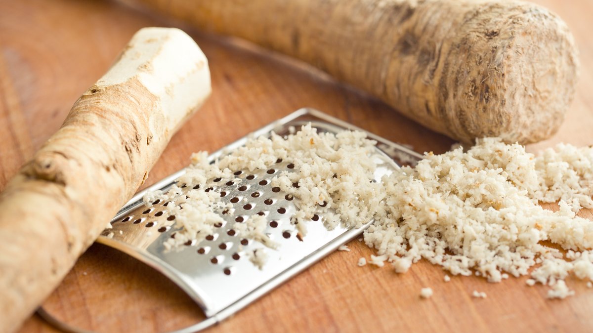 Zwei Stangen Meerrettich, eine Reibe und geriebener Meerrettich auf einem Tisch