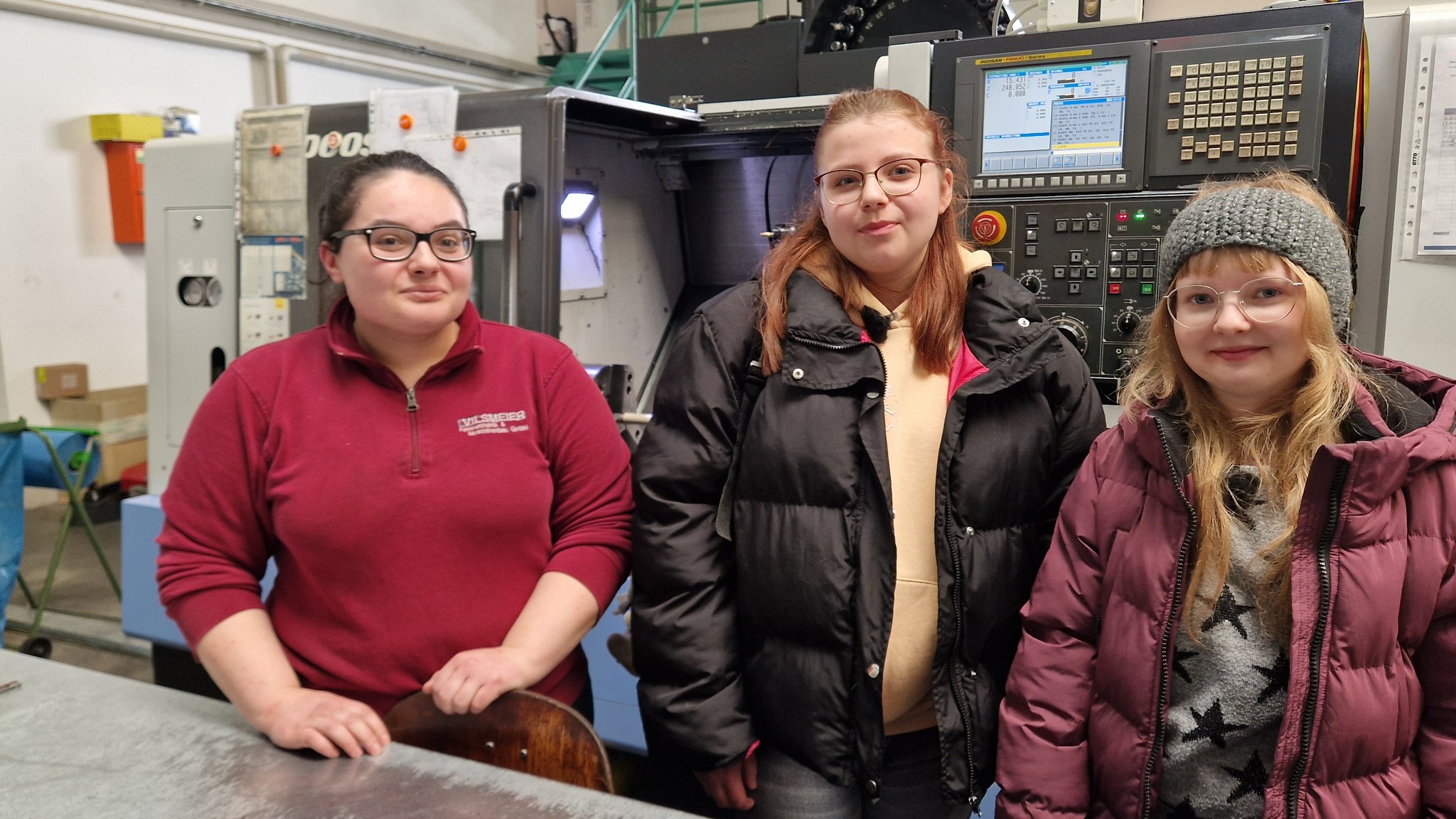 Zwei Schülerinnen stehen neben einer Arbeiterin in einer Maschinenhalle. Hinter ihnen ist eine große Maschine zu sehen. | Bild: Julia Grantner/BR Zwei Schülerinnen stehen neben einer Arbeiterin in einer Maschinenhalle. Hinter ihnen ist eine große Maschine zu sehen.