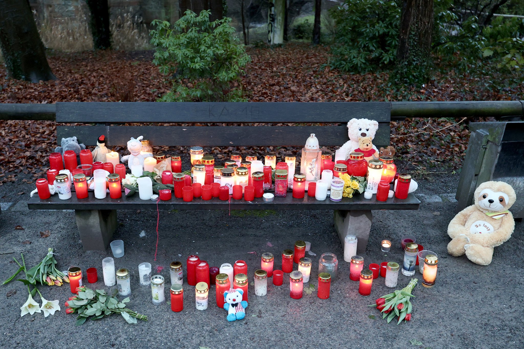 23.01.2025, Bayern, Aschaffenburg: Trauerkerzen, Blumen und Kuscheltiere liegen nach dem tödlichen Angriff in einem Park am Tatort auf einer Bank. In einem Park in Aschaffenburg waren am Vortag ein zweijähriger Junge und ein 41-jähriger Mann getötet sowie zwei weitere Menschen schwer verletzt worden. Foto: Daniel Löb/dpa +++ dpa-Bildfunk +++