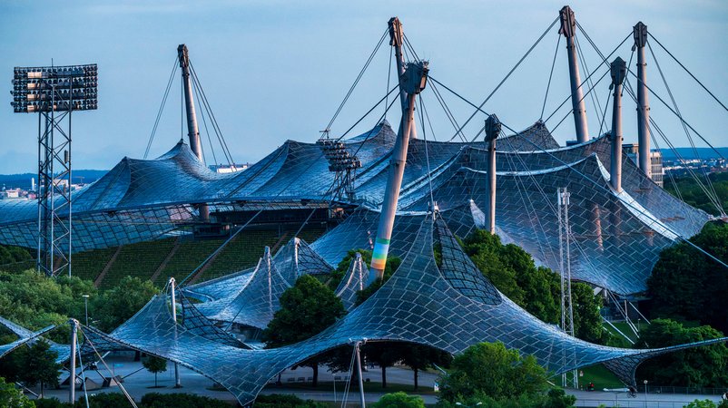 ARCHIV - 19.05.2025, Bayern, München: Die gläserne Zeltkonstruktion des Olympiastadion ragt in den späten Abendstunden in den Himmel. | Bild: Peter Kneffel/dpa ARCHIV - 19.05.2025, Bayern, München: Die gläserne Zeltkonstruktion des Olympiastadion ragt in den späten Abendstunden in den Himmel.