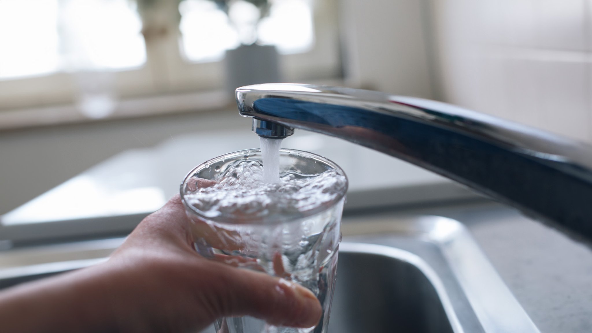 Wasser fließt aus dem Hahn einer Leitung in ein Glas.