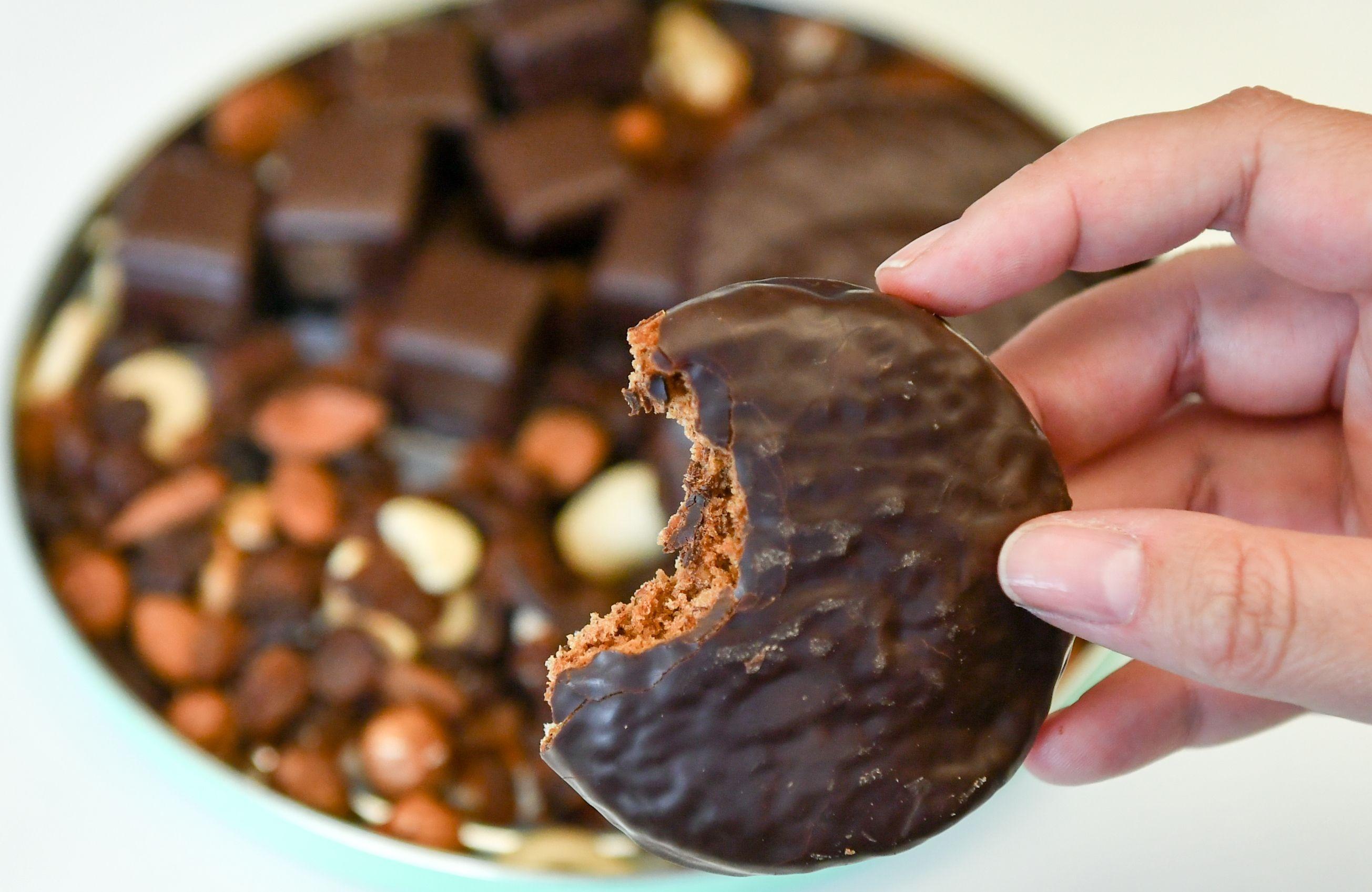 Frauenhand hält angebissenen Lebkuchen mit Schokolade in der Hand.