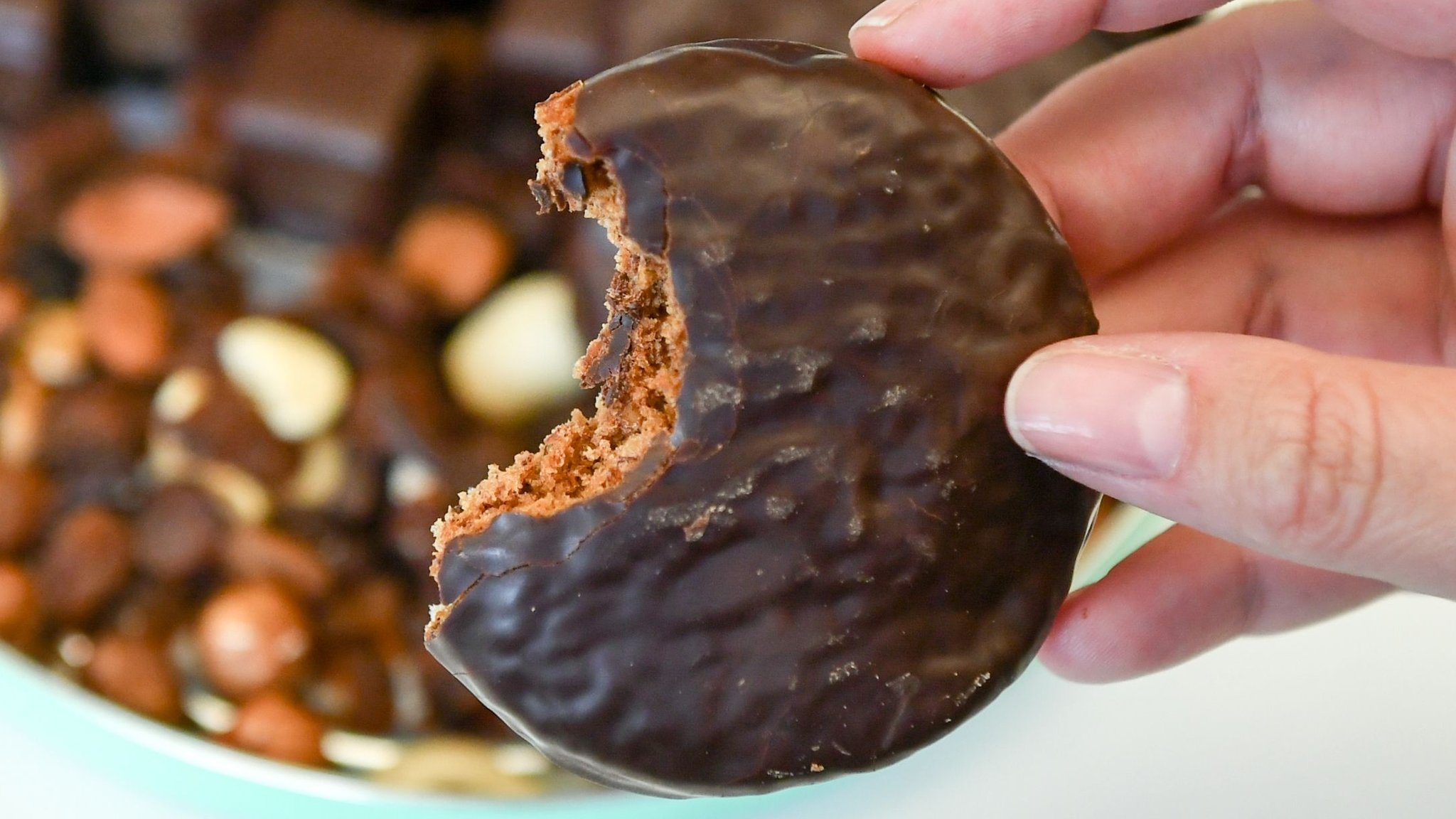 Frauenhand hält angebissenen Lebkuchen mit Schokolade in der Hand.