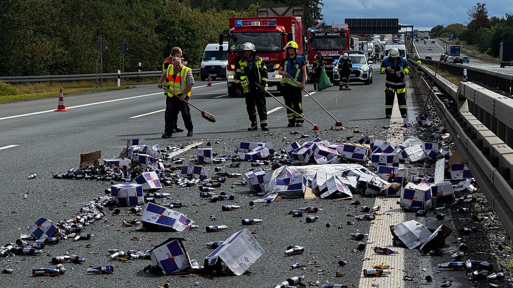 Red-Bull-Flaschen liegen auf der Fahrbahn herum. Im Hintergrund ist ein Stau zu sehen. 
