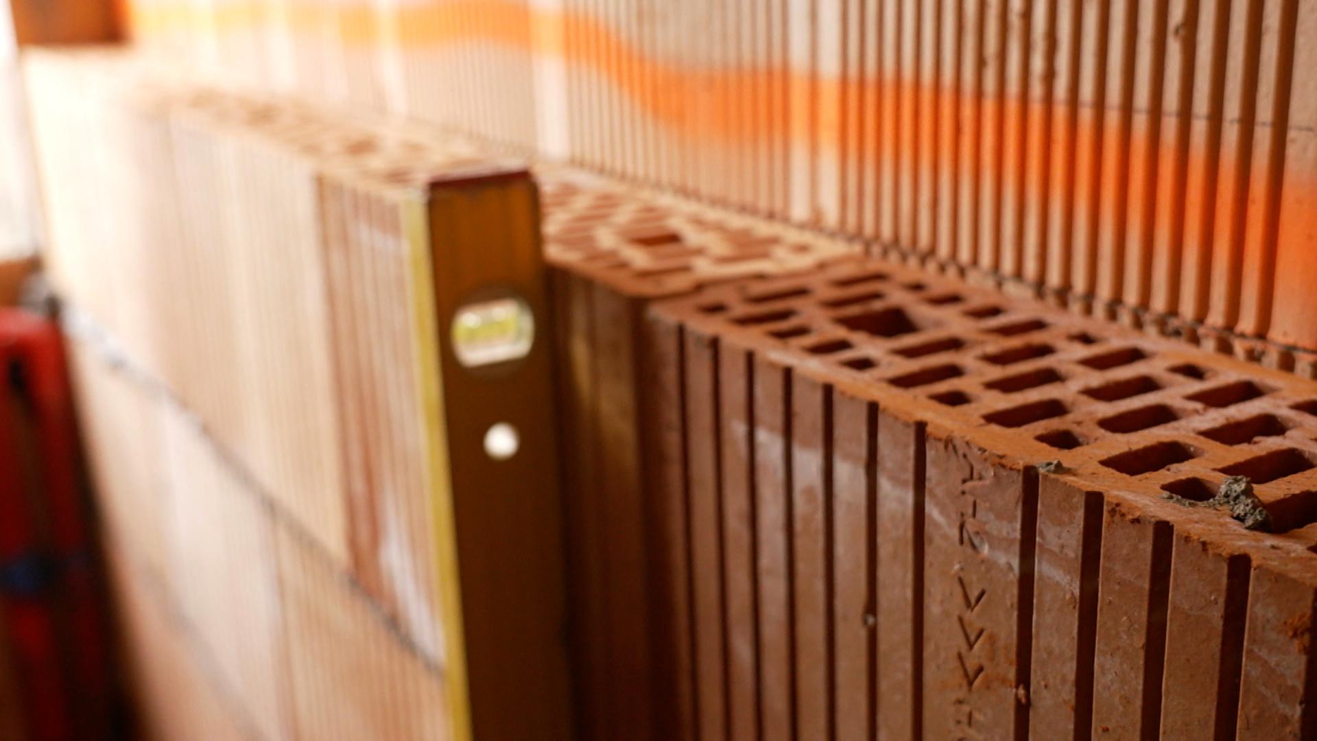 Eine Wasserwaage wird an eine unverputzte Ziegelwand in einem Rohbau gedrückt.