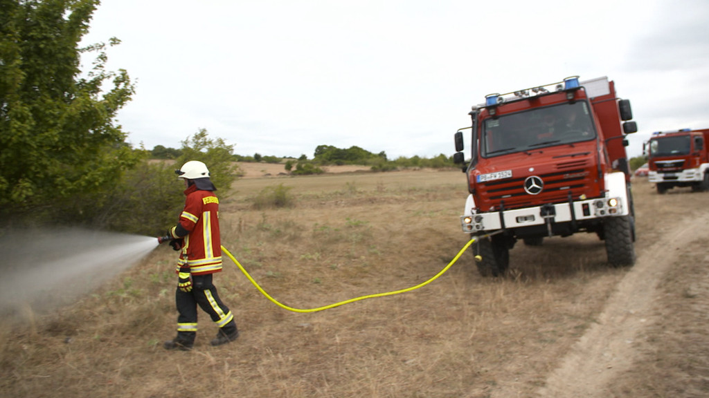 Feuerwehr im Einsatz auf verdorrtem Grasland.