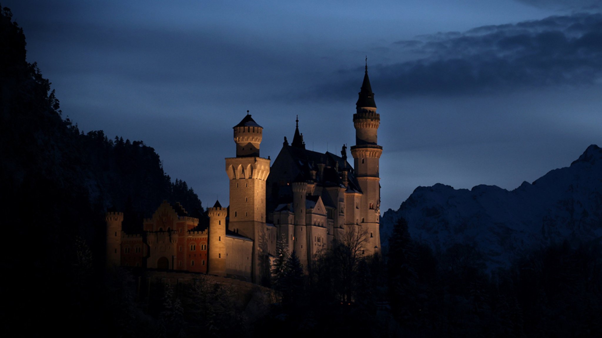 Bayern, Schwangau: Das Schloss Neuschwanstein steht nach Sonnenuntergang zur Blauen Stunde vor dem Panorama der Alpen.