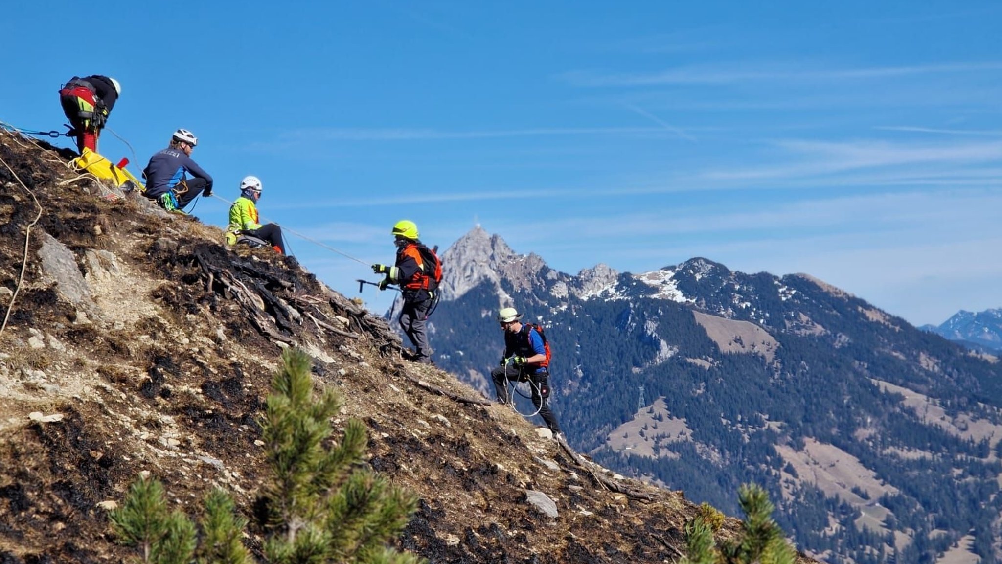 Fünf Bergsteiger steigen einen Hang hoch; dahinter Bergkulisse