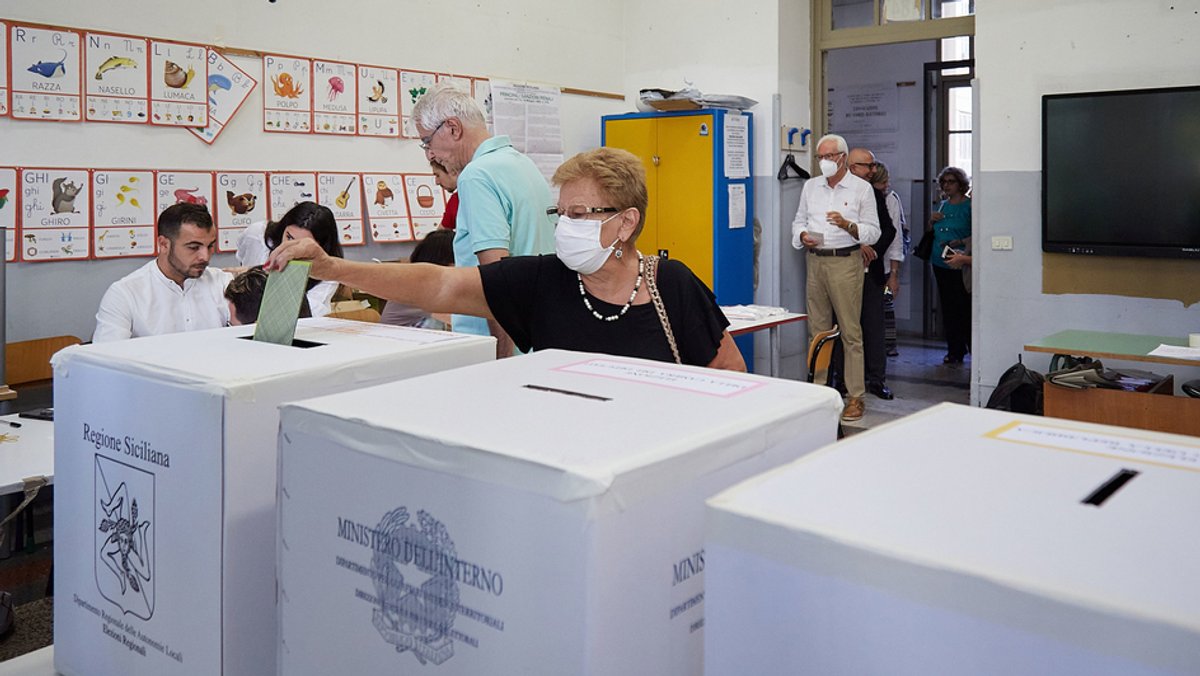 Eine ältere Frau mit medizinischer Maske steckt ihren Stimmzettel in Palermo in eine Wahlurne.