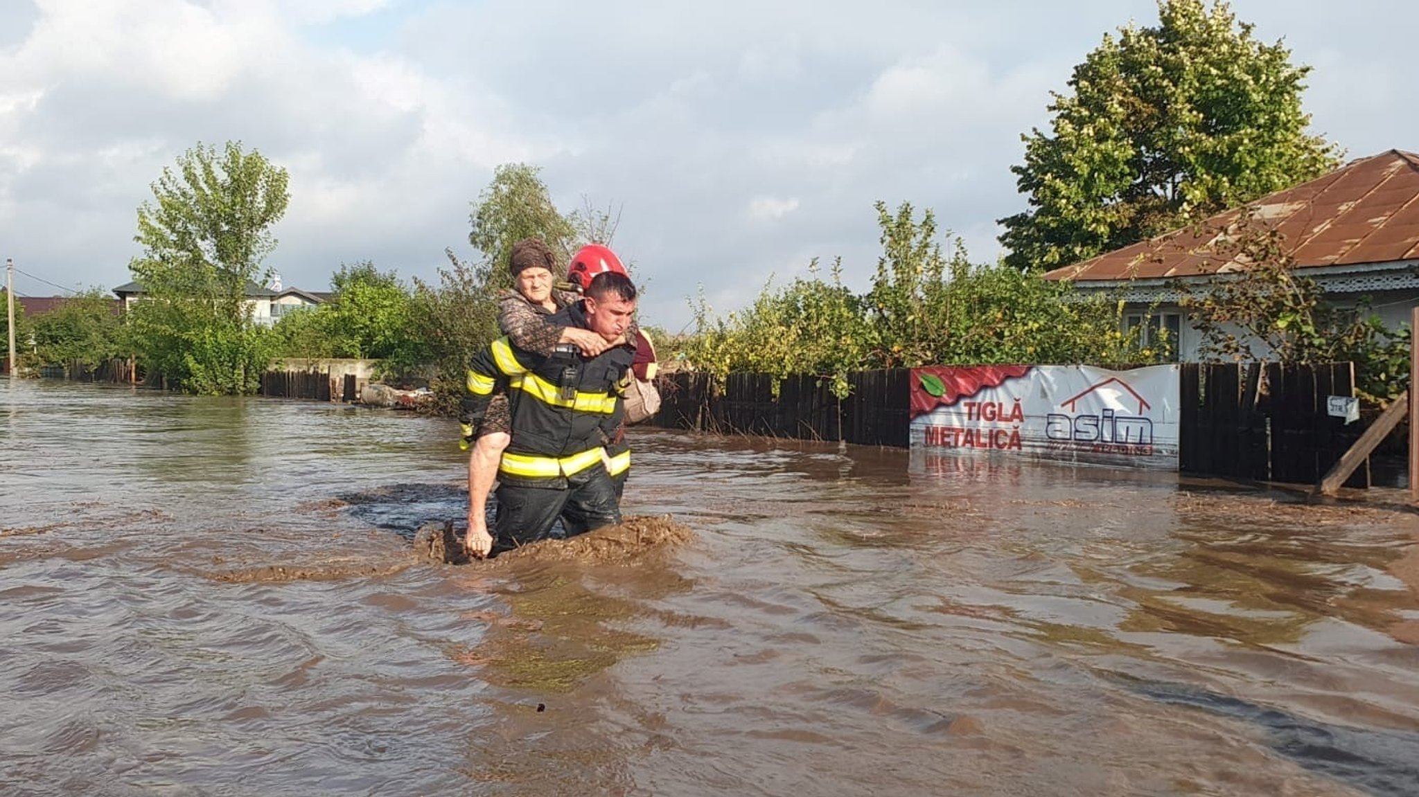 Eine Einsatzkraft trägt eine ältere Dame auf dem Rücken durch die Fluten. Das Wasser steht ihm fast bis zur Hüfte, die Anstrengung ist ihm anzusehen. Viele Menschen in Rumänien haben durch das Hochwasser all ihr Hab und Gut verloren.