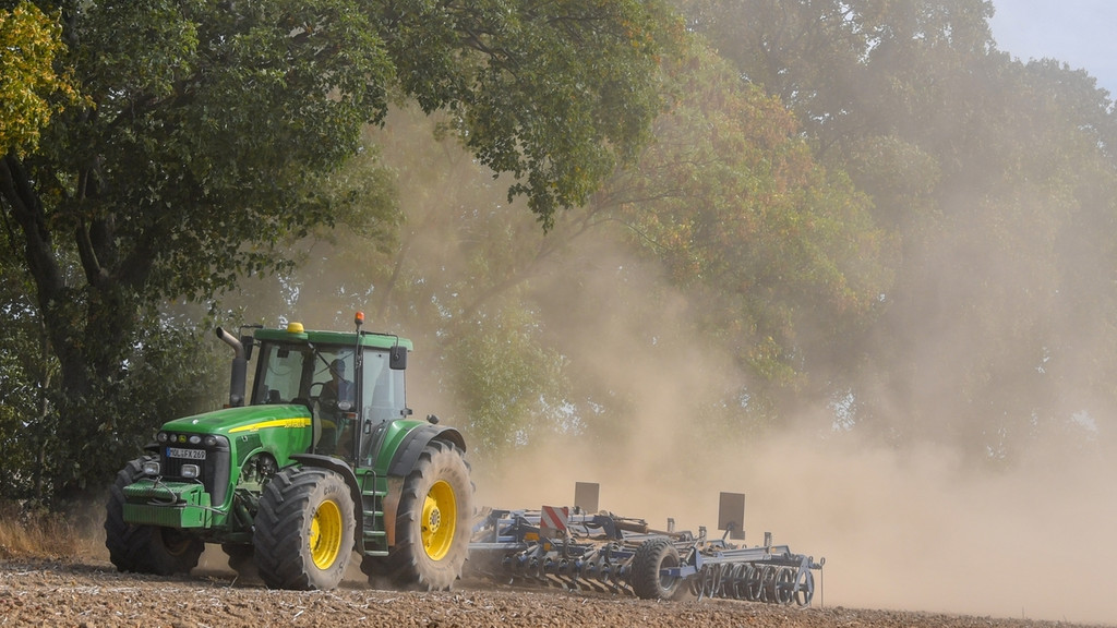 Ein Landwirt bearbeitet mit dem Traktor den trocken Boden und wirbelt dabei viel Staub auf