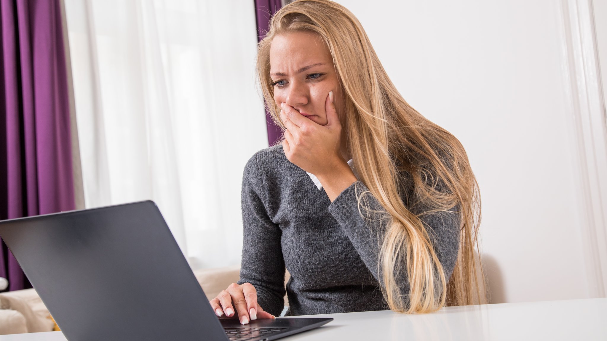 Frau sitzt vor ihrem Laptop und blickt konzentriert in den Bildschirm.