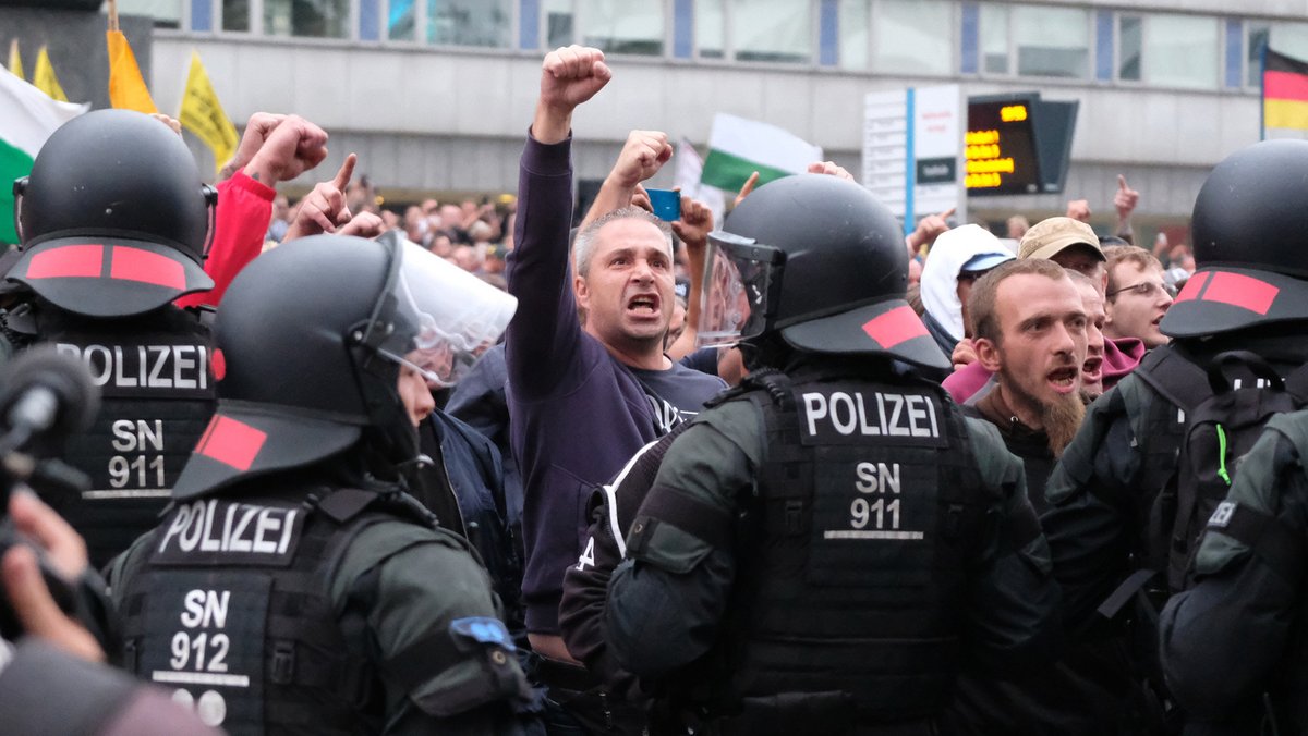 Rechte Demonstranten stehen in Chemnitz vor dem Karl-Marx-Monument, davor sind Polizisten