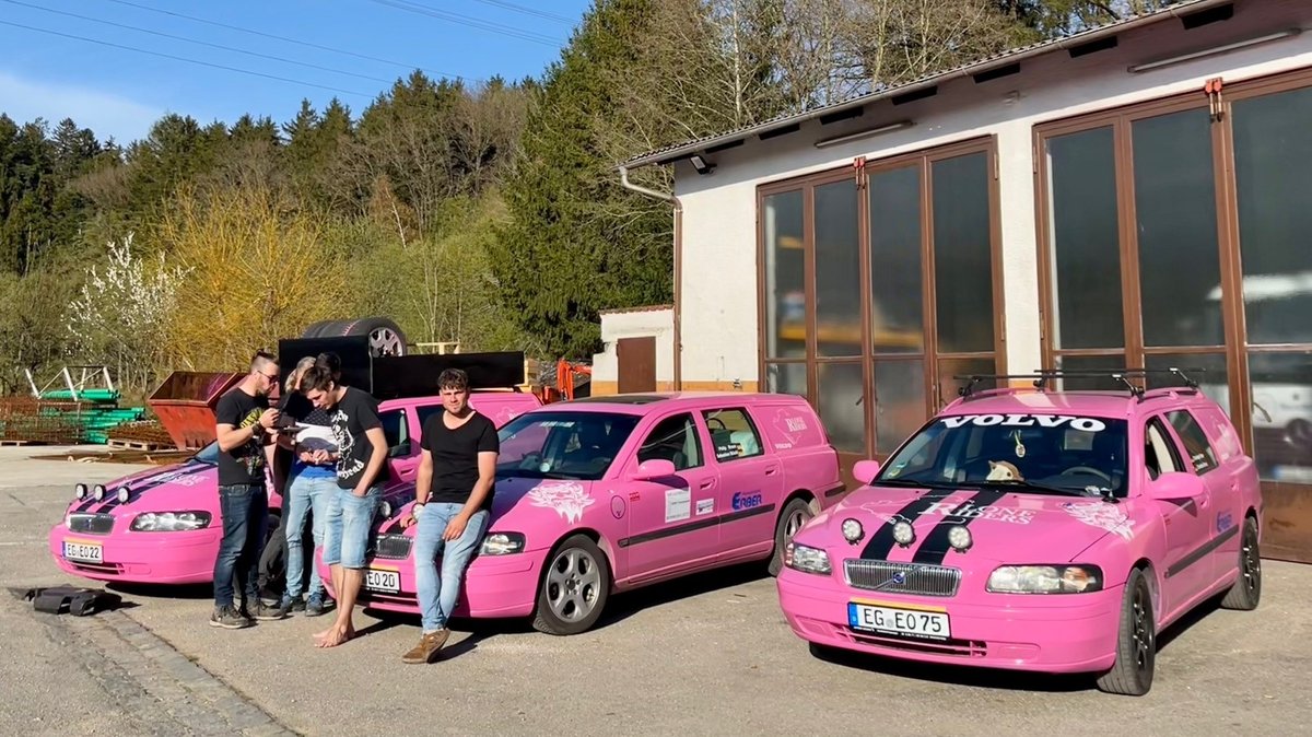 Männer vor pinkfarbenen Autos