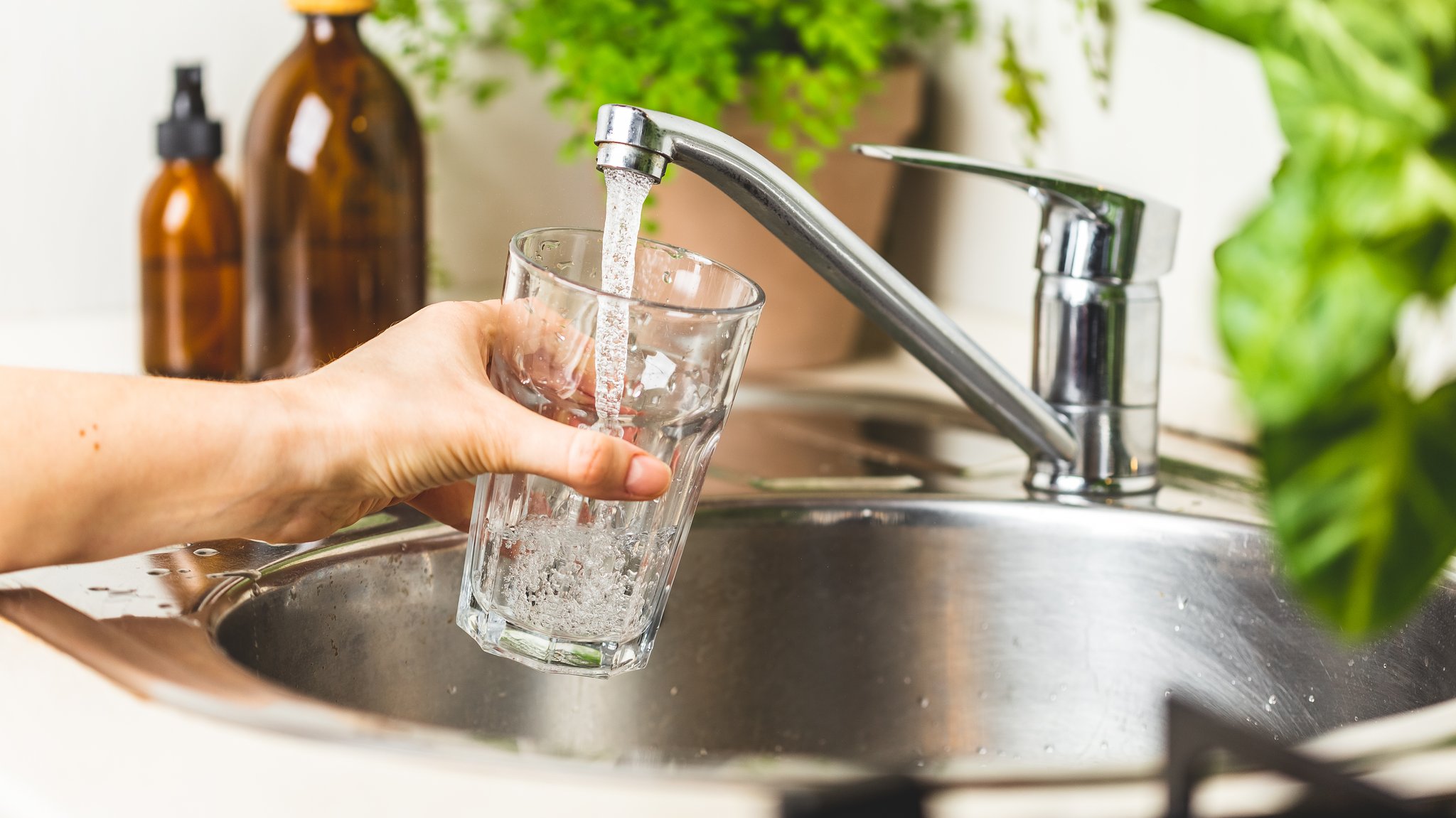 Eine Frauenhand hält ein Trinkglas unter den Wasserhahn und füllt dieses mit fließendem, klarem Wasser.