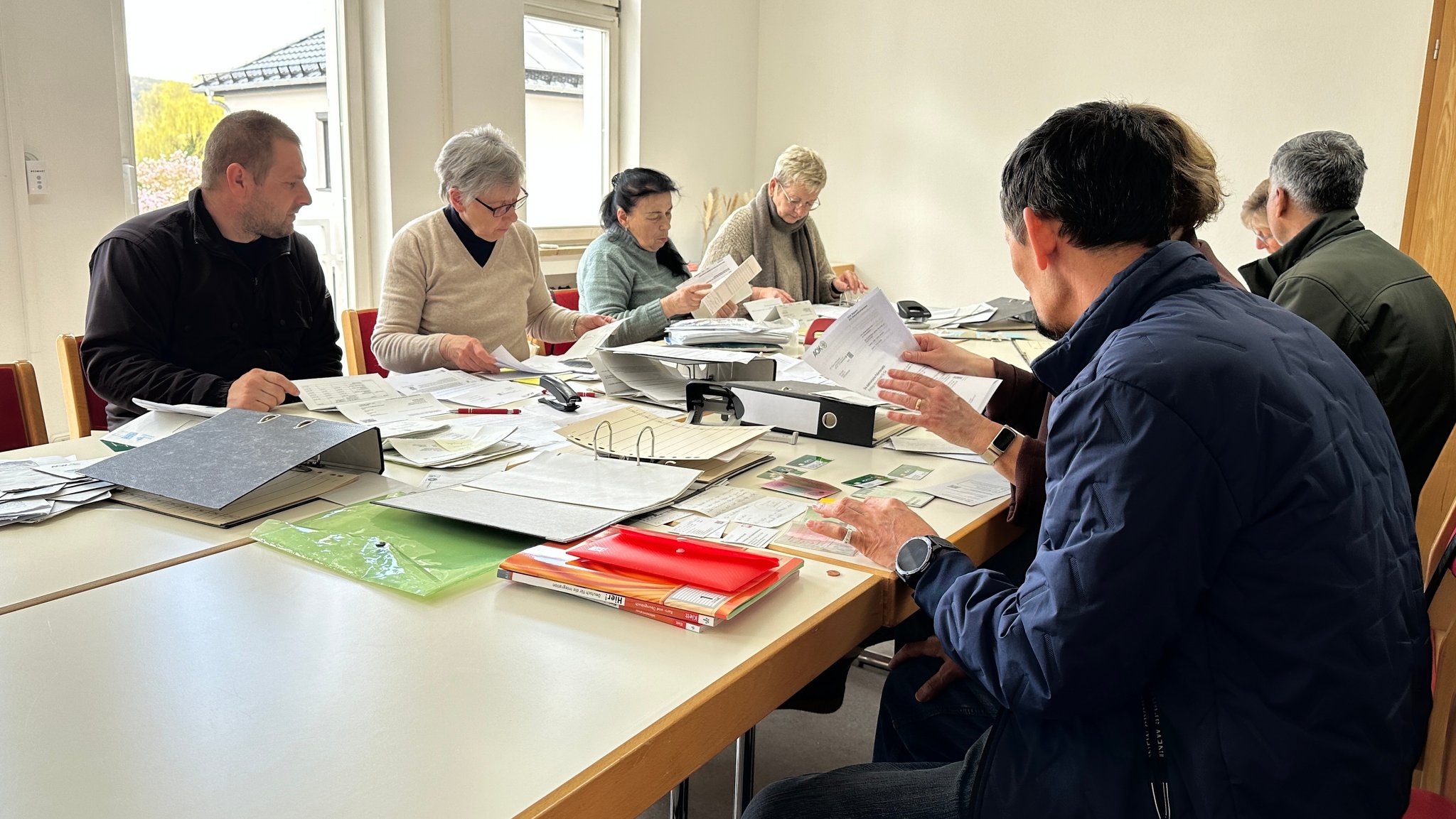 Ehrenamtliche und Geflüchtete sitzen zusammen an einem Tisch und ordnen Dokumente.