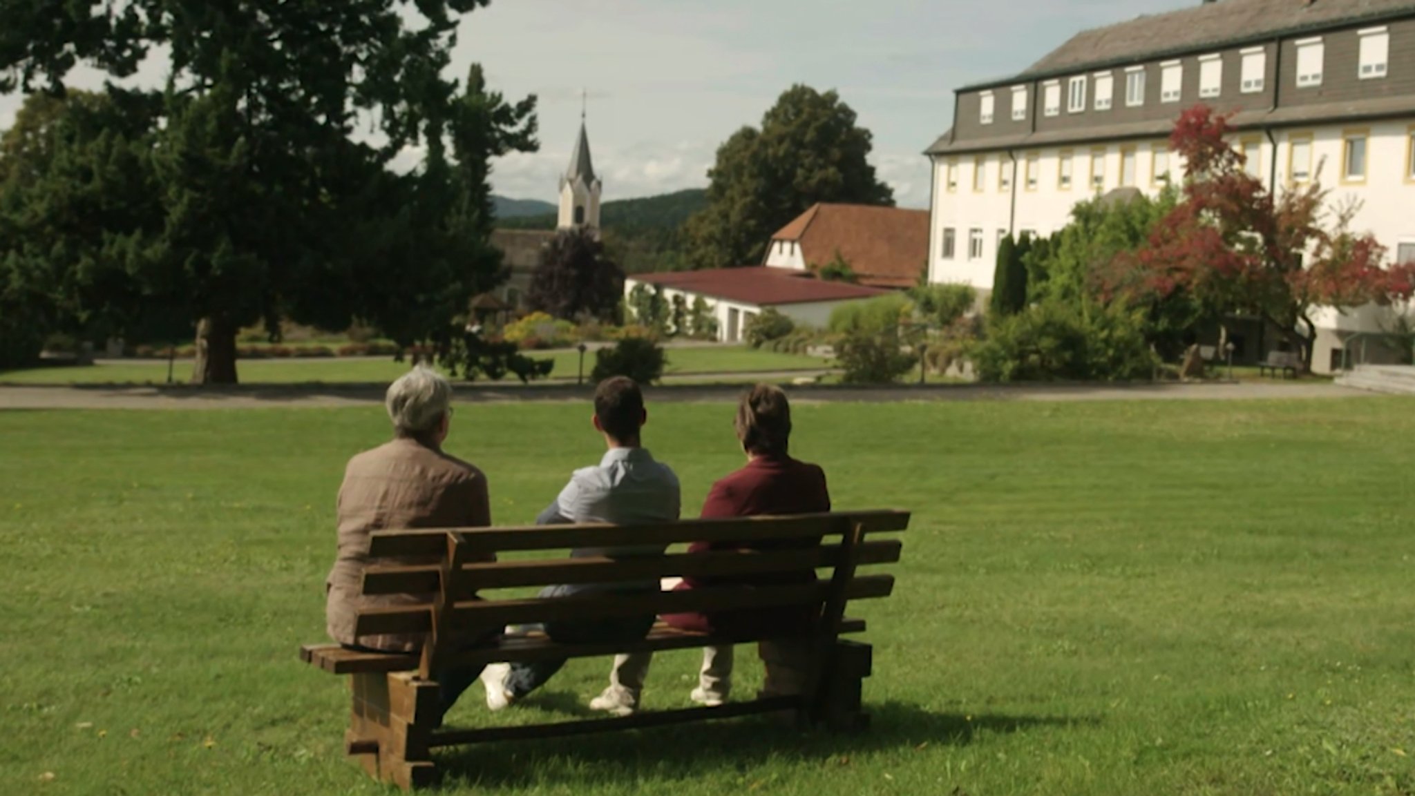Drei Anwohner sitzen auf einer Bank im Klosterhof und blicken auf die Klostergebäude mit der Kapelle. | Bild: Bayerischer Rundfunk 2025 Drei Anwohner sitzen auf einer Bank im Klosterhof und blicken auf die Klostergebäude mit der Kapelle.