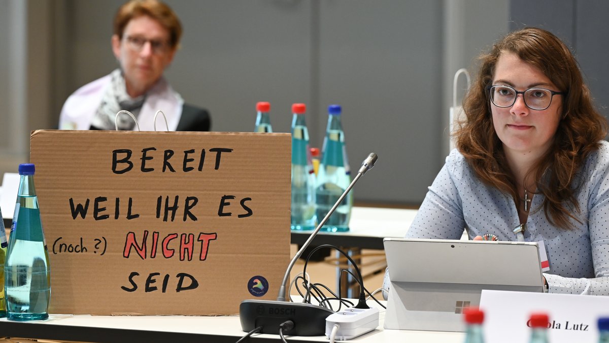 Carola Lutz vom Bund der Deutschen Katholischen Jugend sitzt während der Zweiten Synodalversammlung der katholischen Kirche neben einem Plakat mit der Aufschrift "Bereit weil Ihr es (noch?) nicht seid".